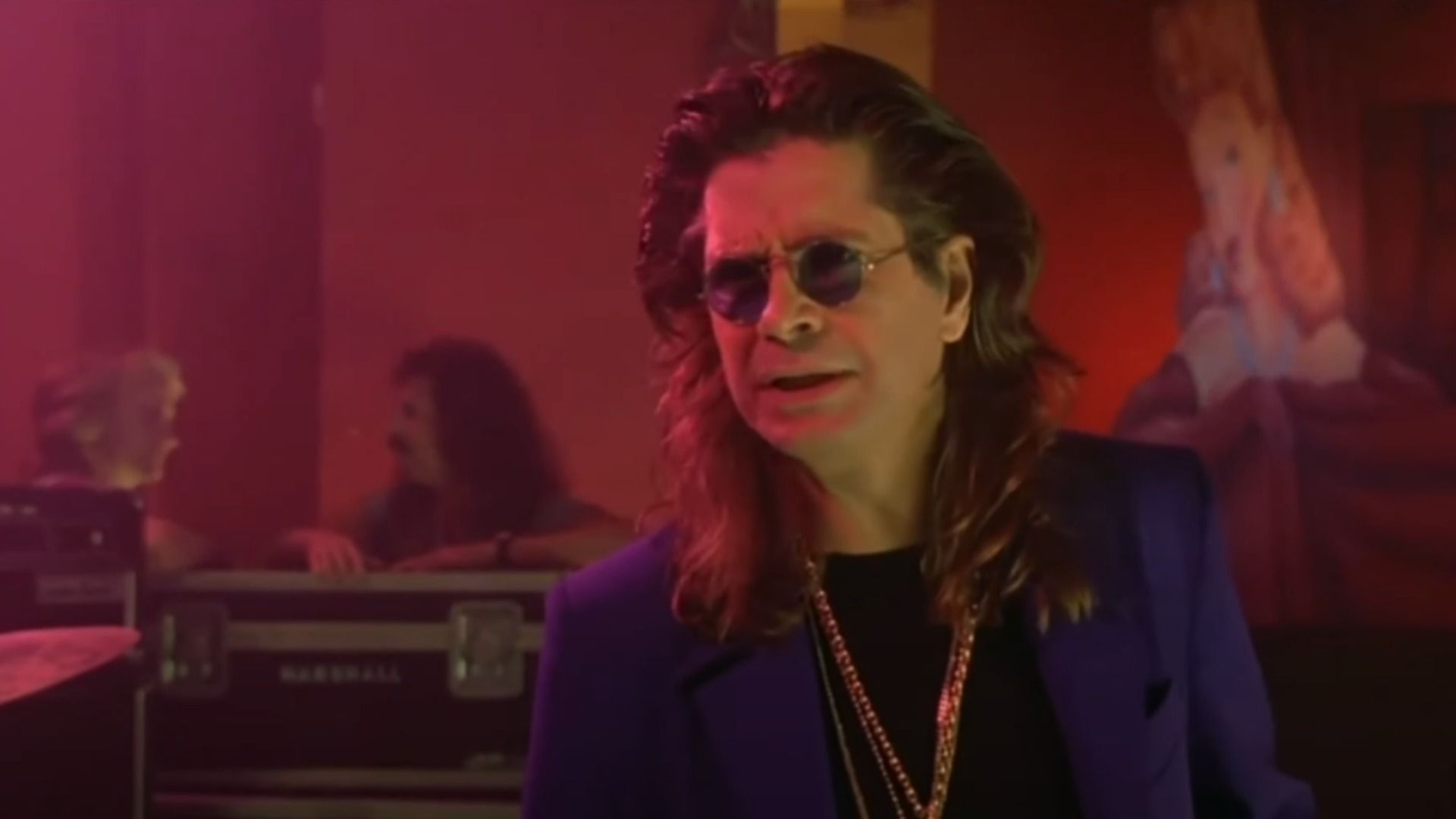 El cantante Ozzy Osbourne con blazer azul y cadena dorada de pie en el escenario