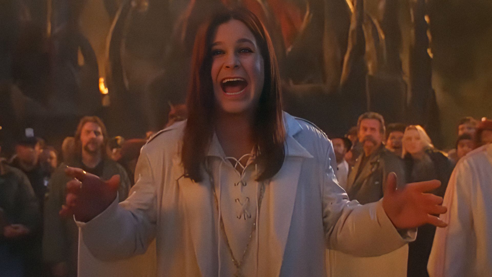 El cantante Ozzy Osbourne con chaqueta blanca extiende los brazos y sonríe