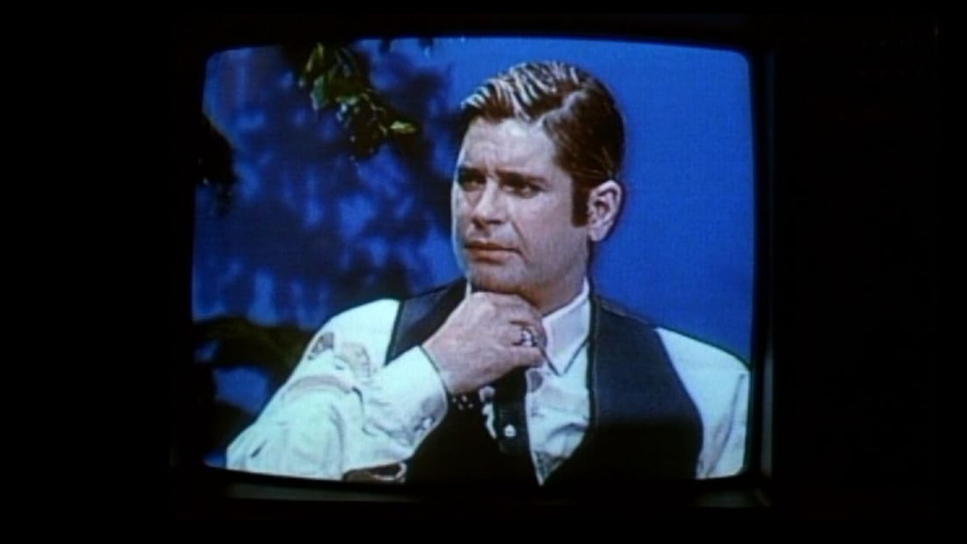 El cantante Ozzy Osbourne con cabello corto sentado en una mesa vistiendo camisa blanca y chaleco negro