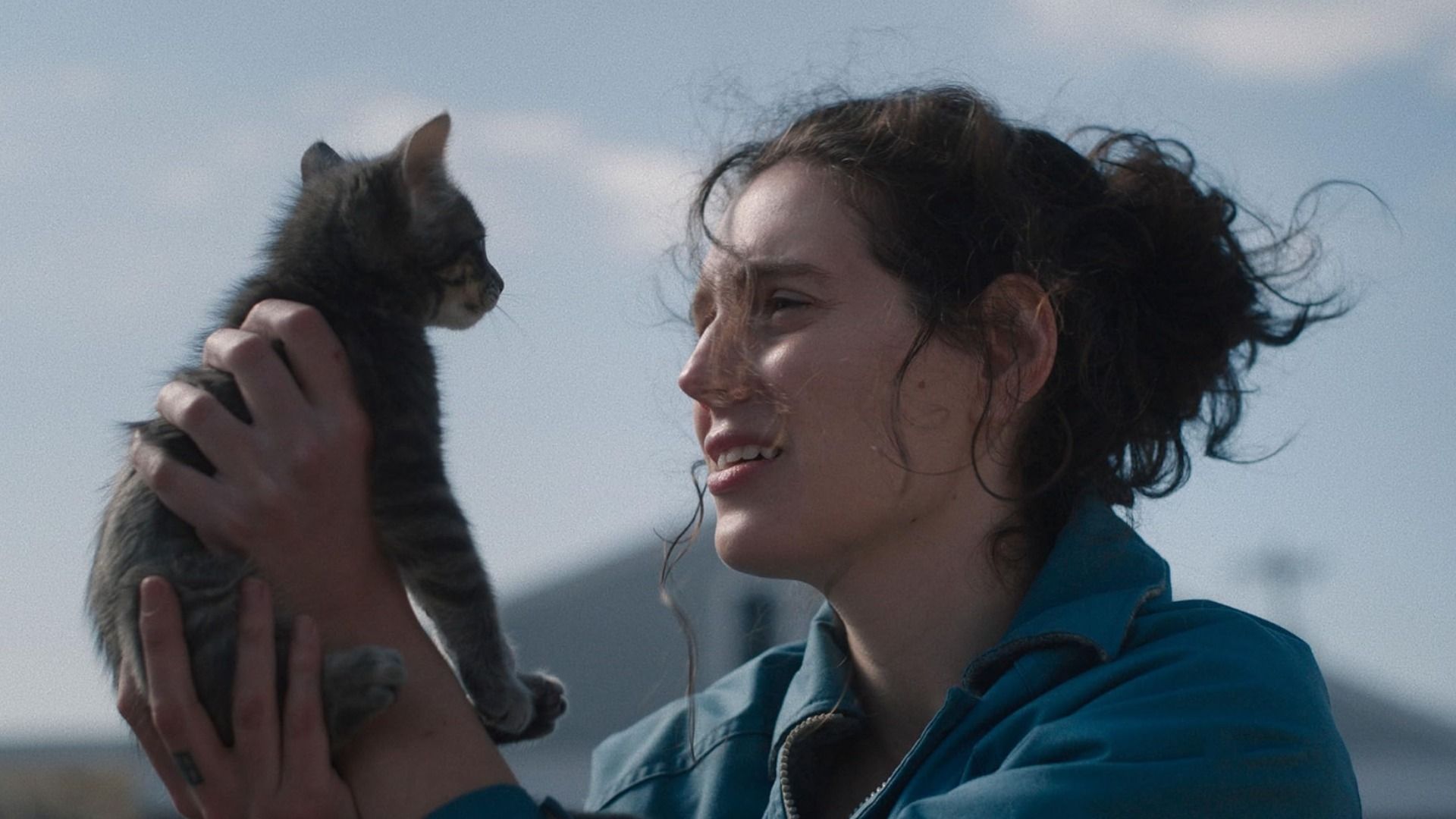 Chica con chaqueta azul sosteniendo un gatito gris