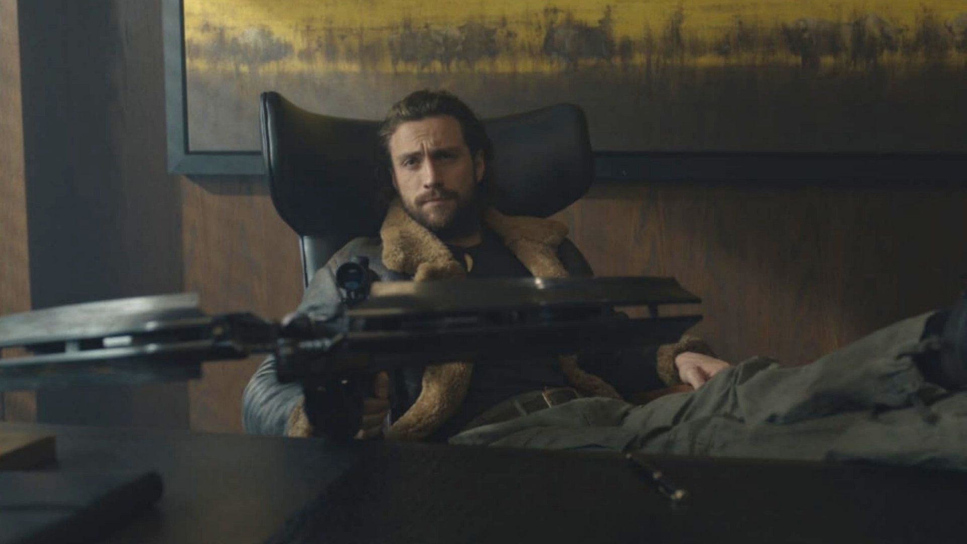 El actor Aaron Taylor-Johnson está sentado en una mesa con una ballesta en las manos