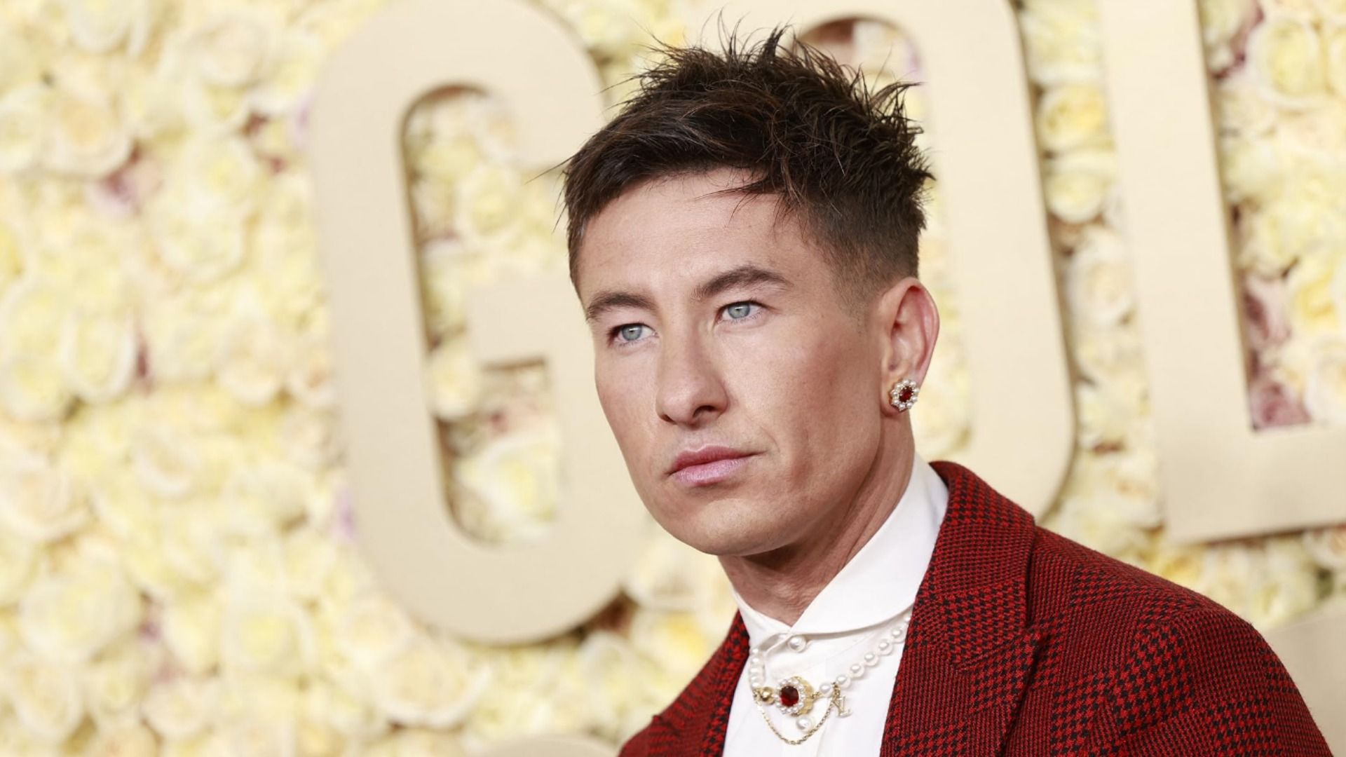 El actor Barry Keoghan con chaqueta roja y pendiente de pie contra un fondo amarillo