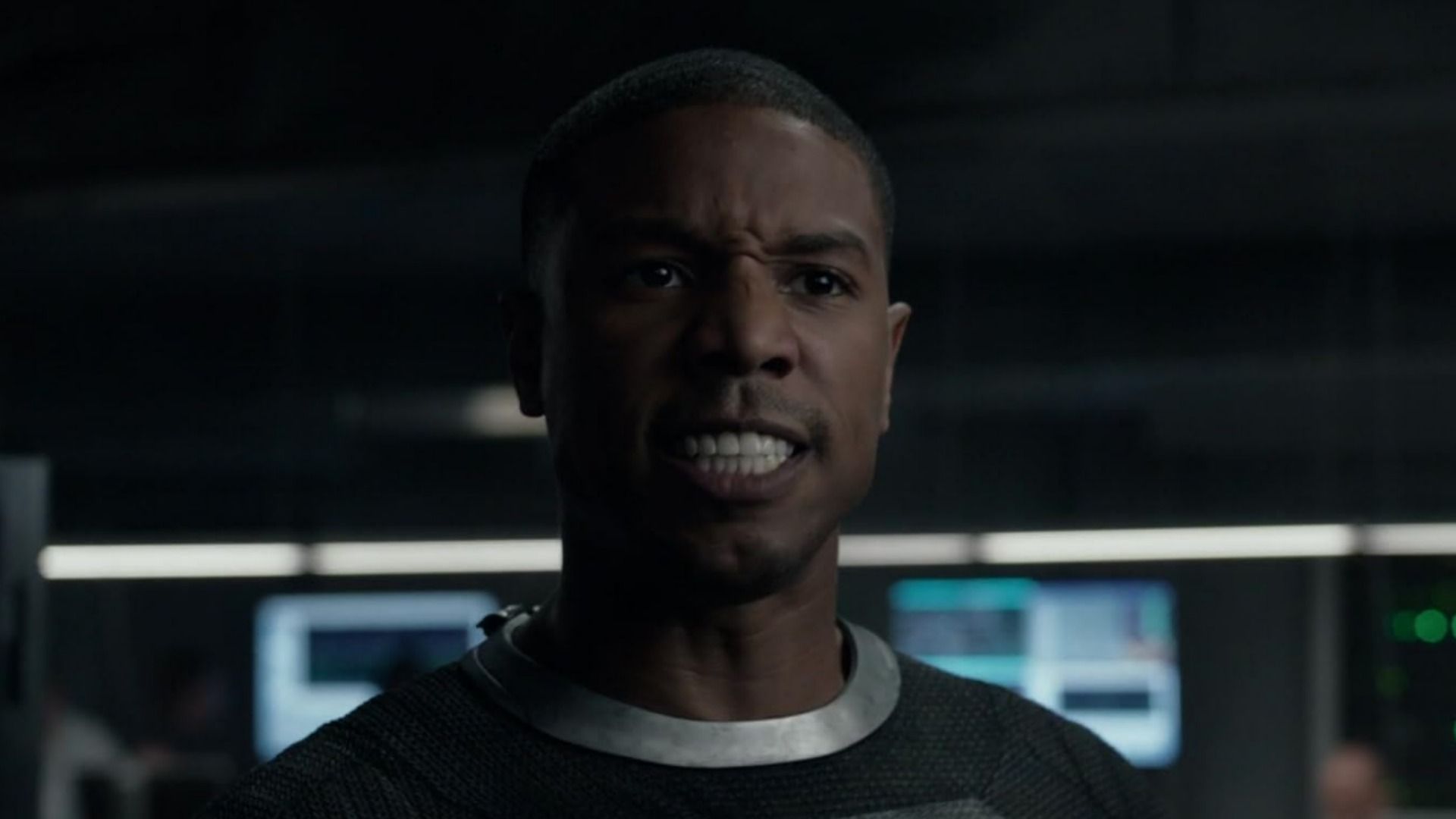 El actor Michael B. Jordan con traje gris y expresión enojada contra un fondo borroso
