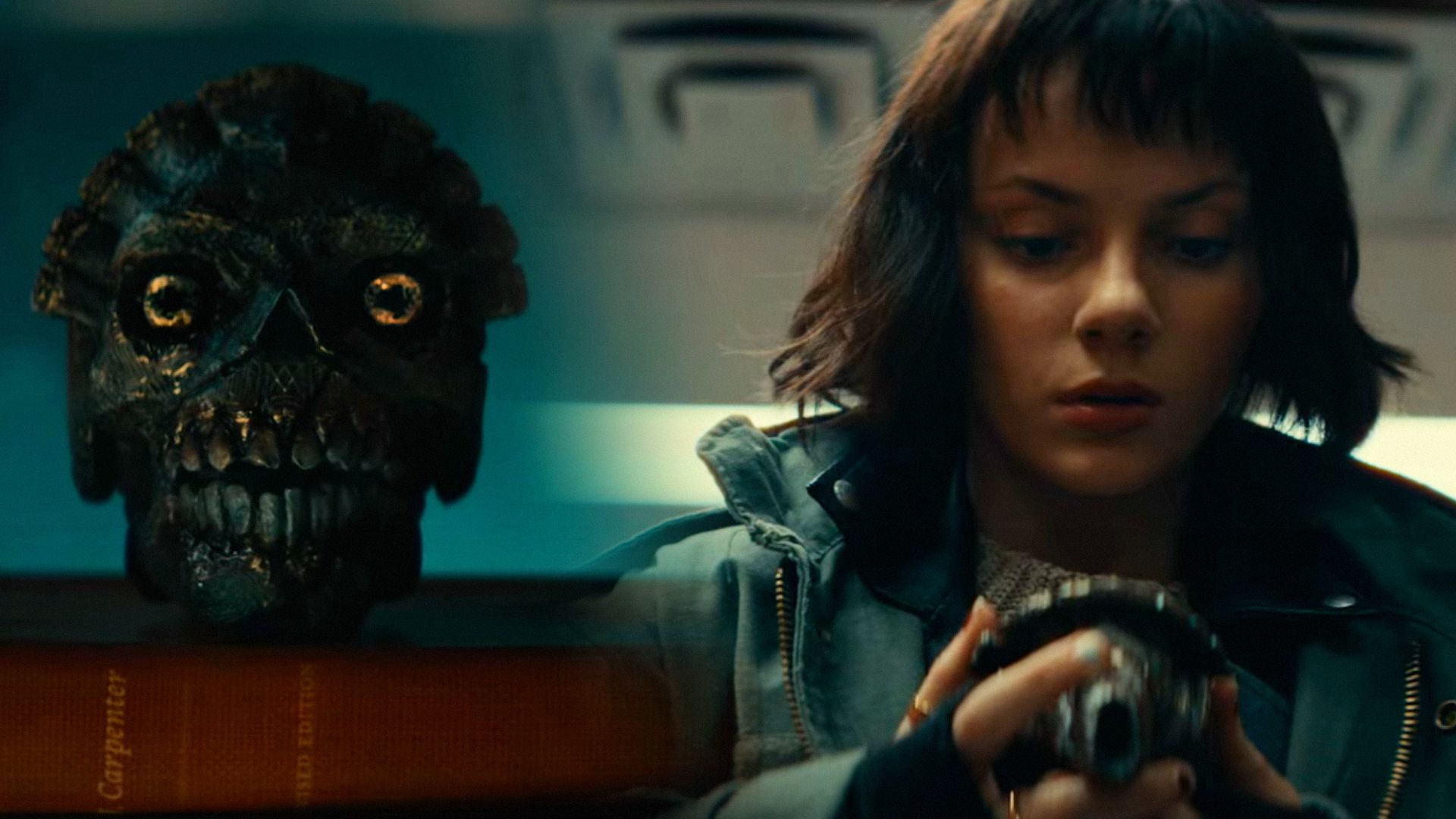 Calavera de metal, a la derecha la actriz Dafne Keen con chaqueta verde sostiene esta calavera en sus manos