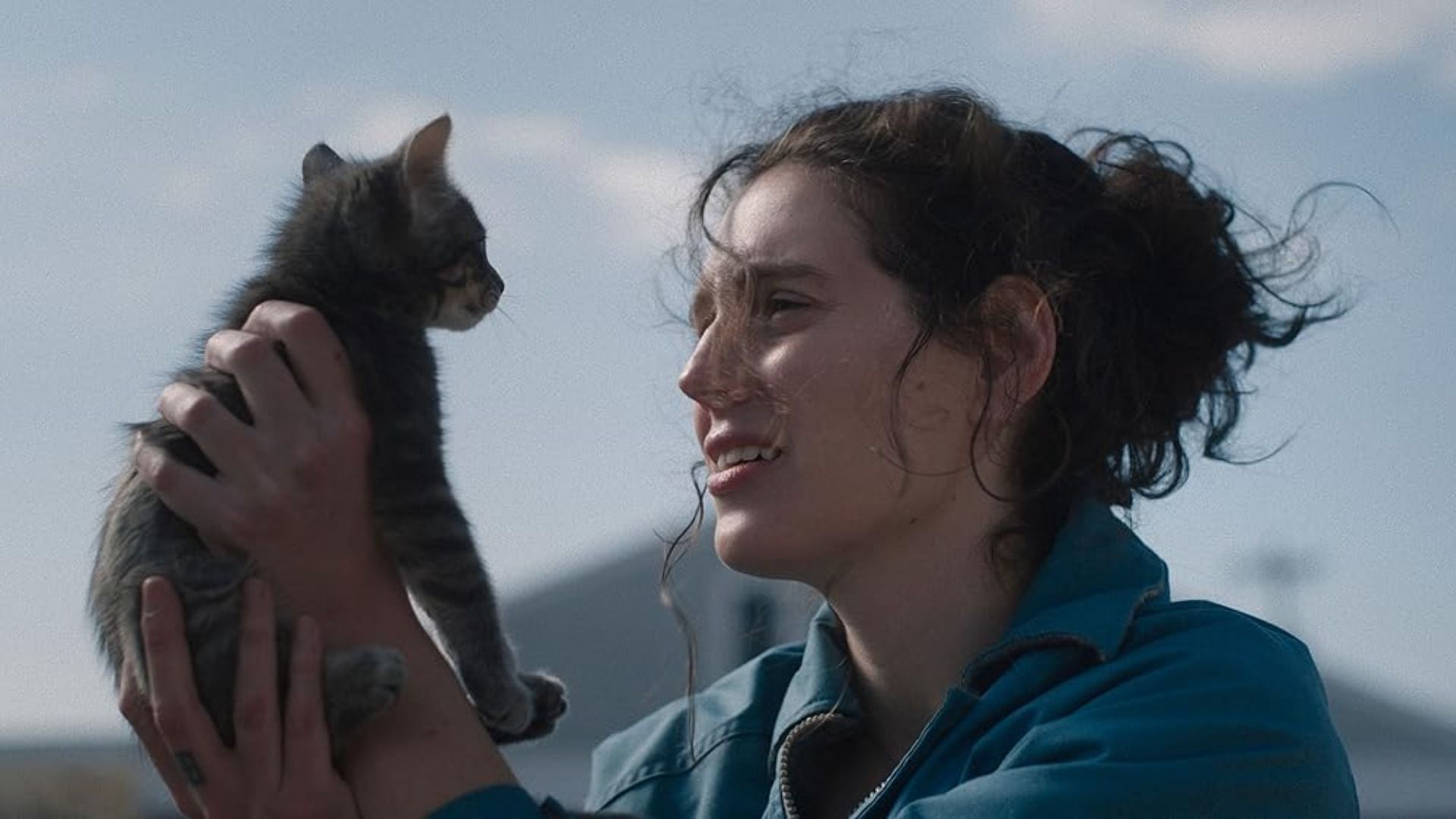 Una chica con chaqueta azul sostiene un gatito y lo mira