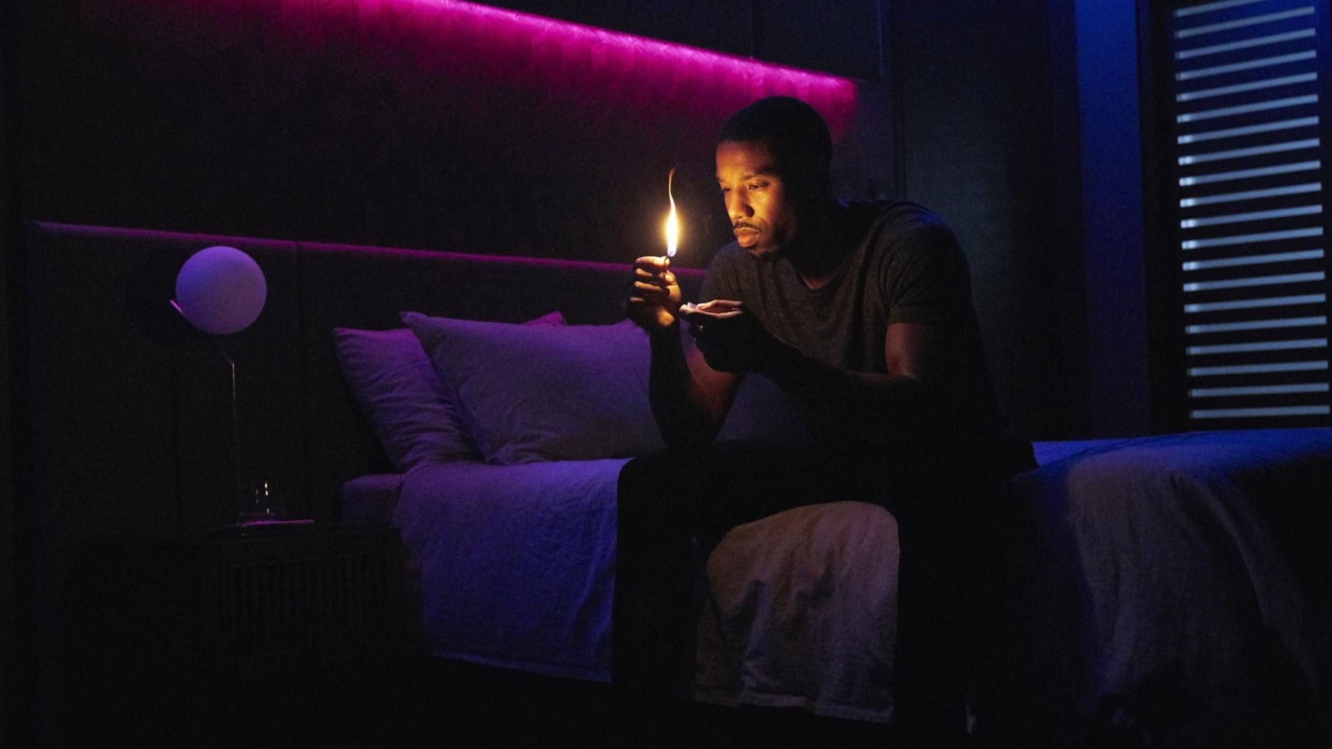 El actor Michael B. Jordan está sentado en una cama con una cerilla en las manos