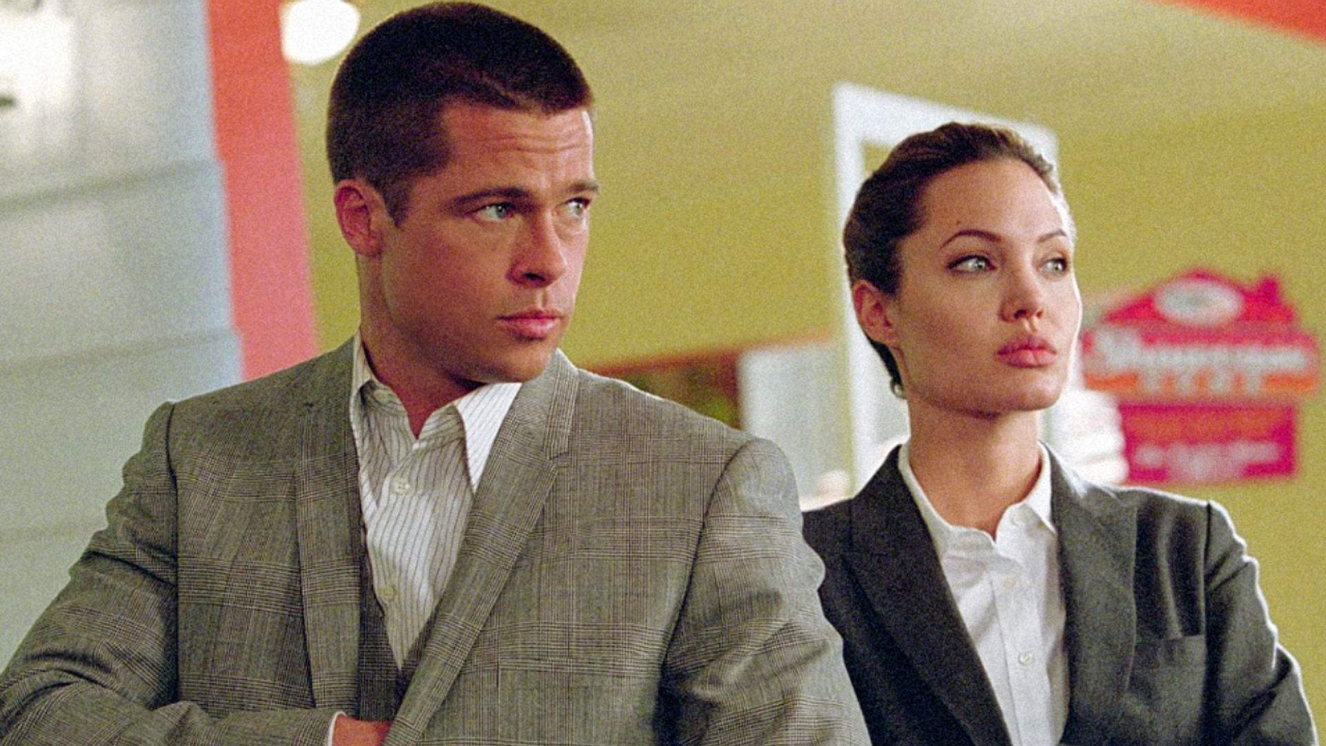 El actor Brad Pitt con blazer gris y corte de pelo corto, la actriz Angelina Jolie con blazer gris y camisa blanca