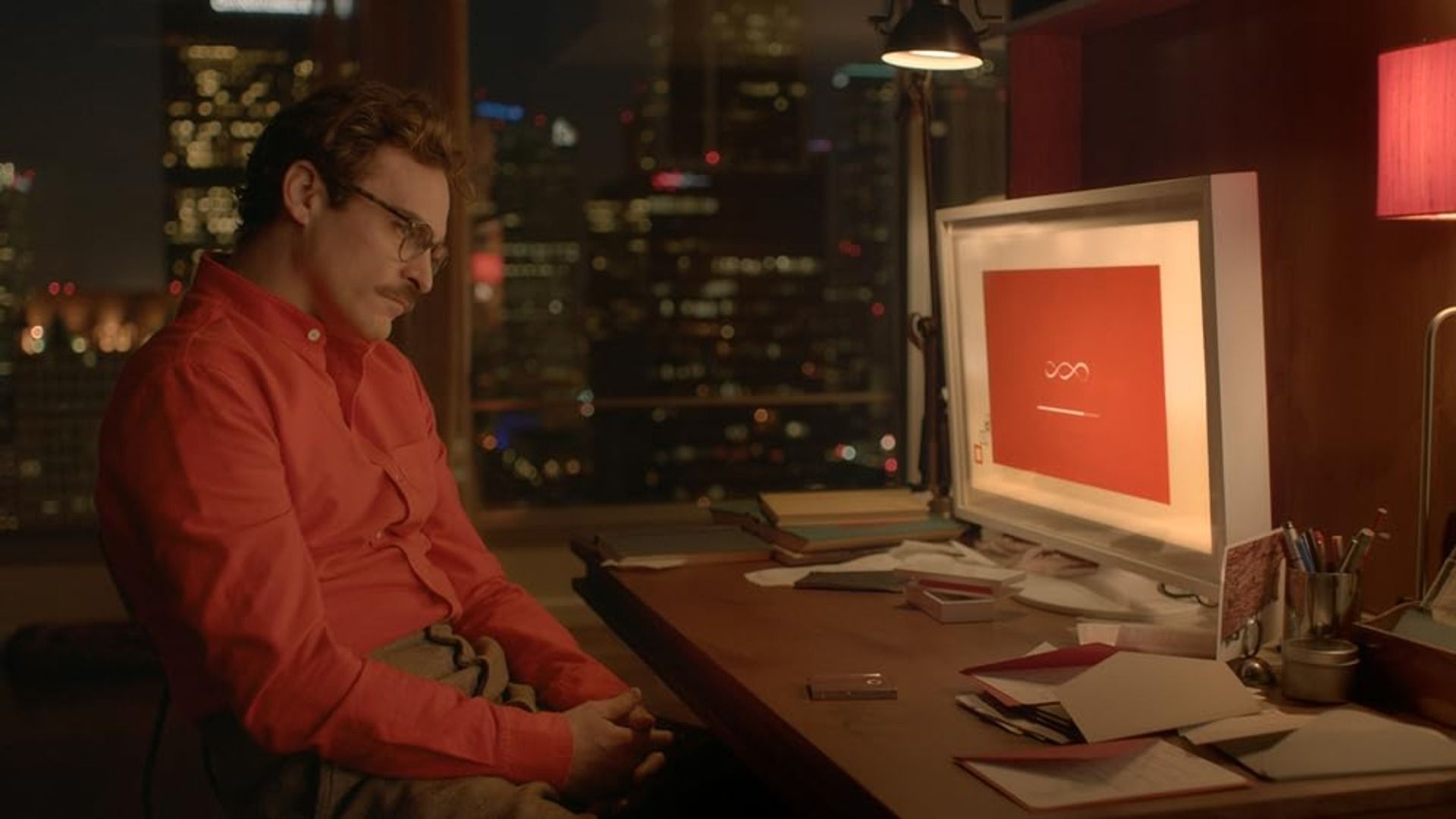 El actor Joaquin Phoenix con una camisa roja sentado en una mesa con un ordenador