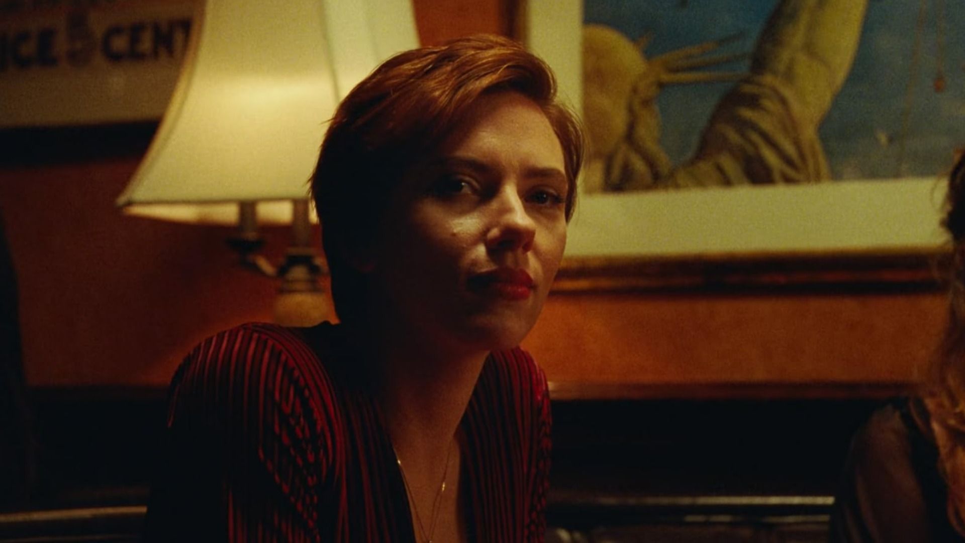 La actriz Scarlett Johansson con una blusa roja sentada junto a una lámpara
