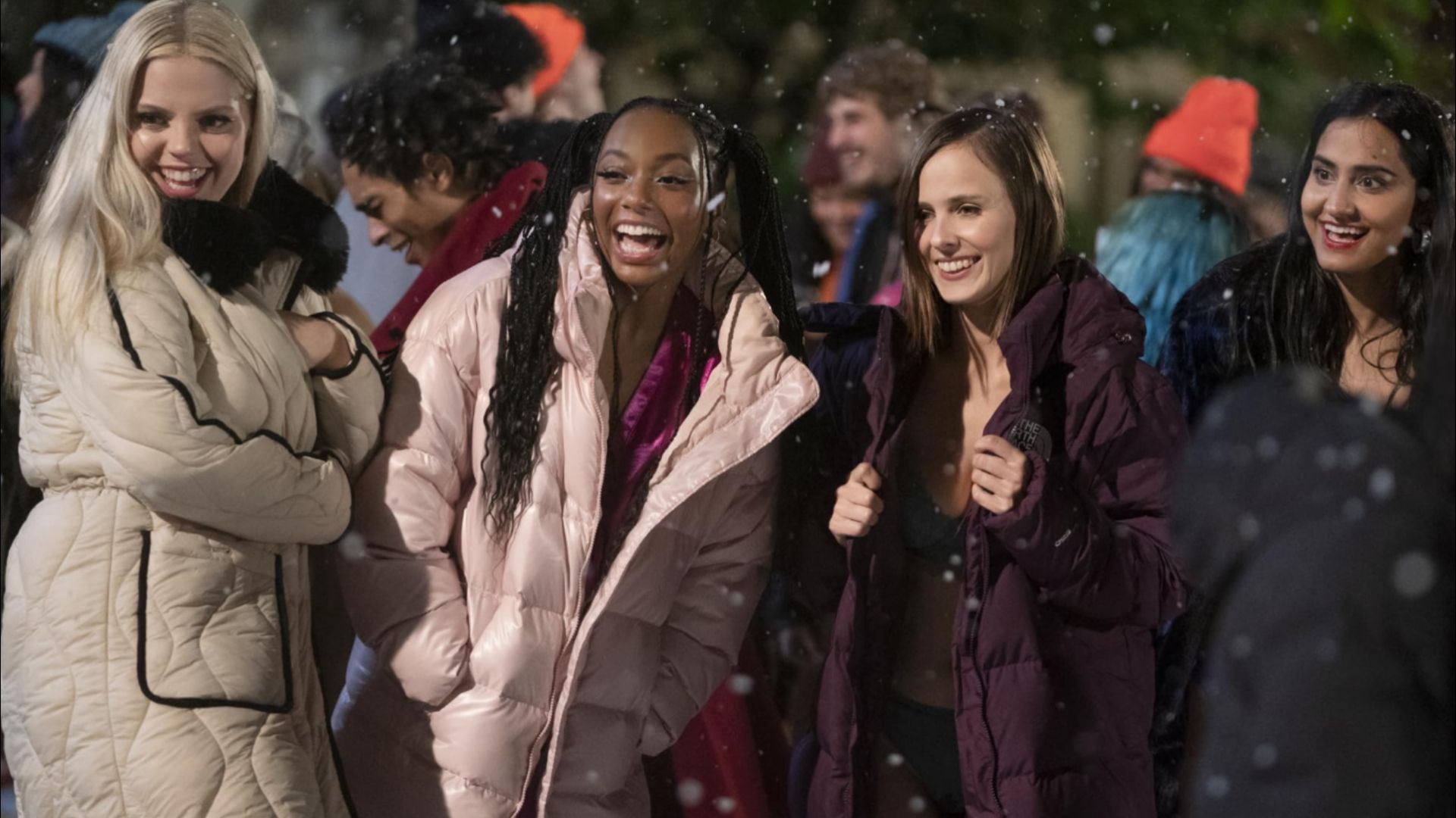 Cuatro chicas de pie con chaquetas coloridas contra un fondo de copos de nieve cayendo