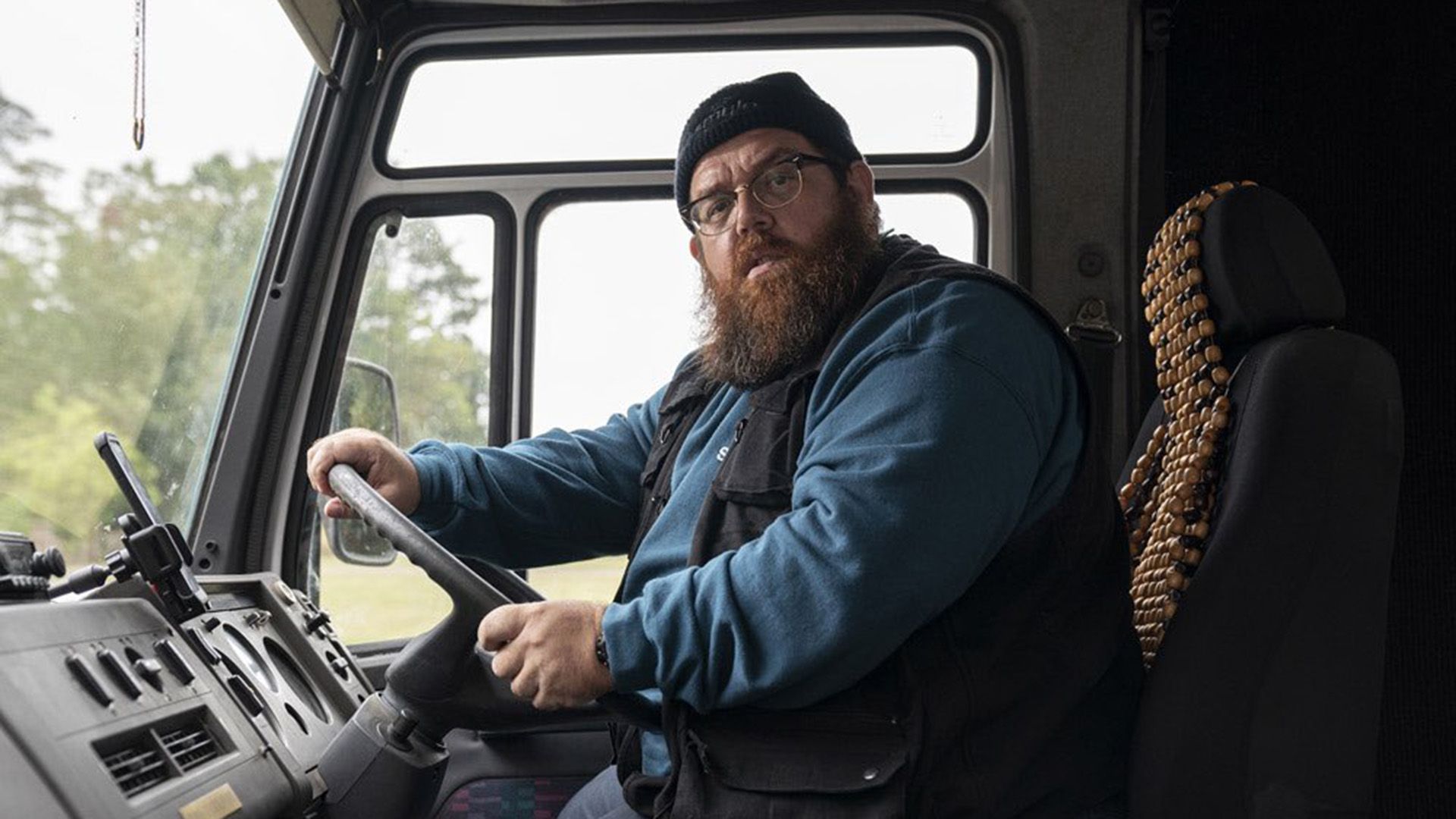 Nick Frost con gafas y sombrero sentado al volante de un camión, mirando a la cámara