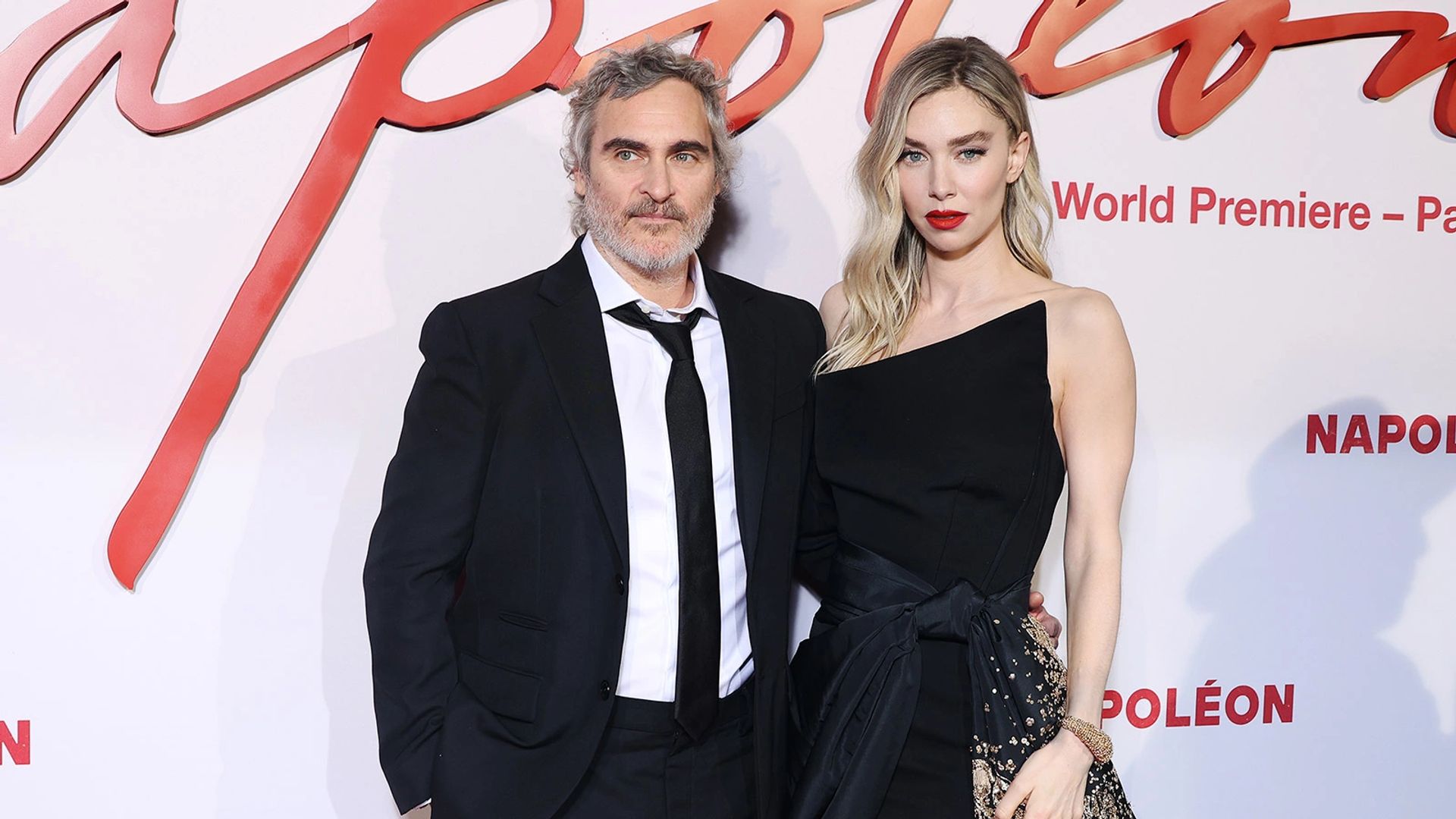 Joaquin Phoenix y Vanessa Kirby posan en la alfombra roja del estreno de la película "Napoleon", ambos vistiendo elegantes trajes negros
