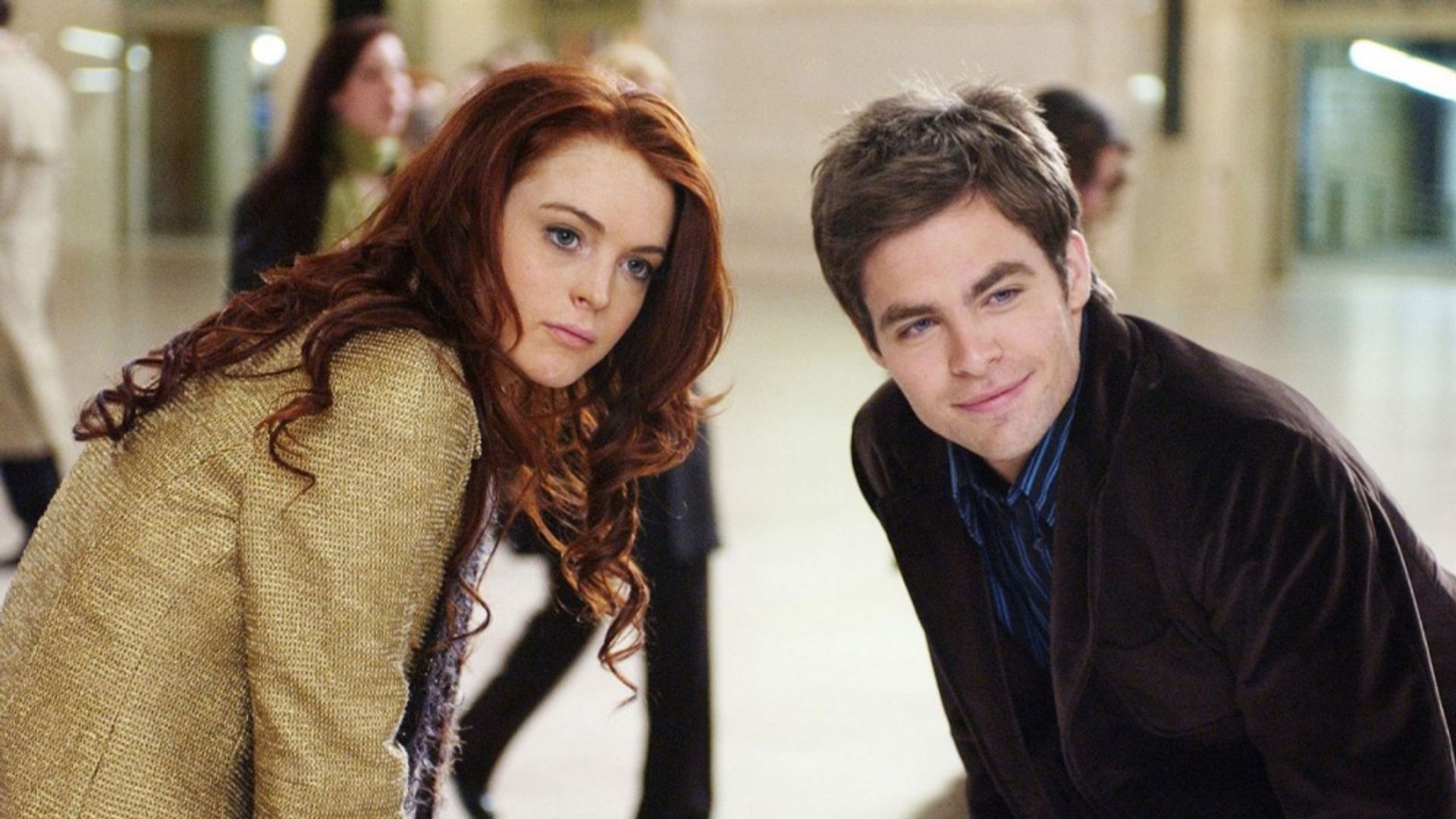 Lindsay Lohan y Chris Pine están parados lado a lado, inclinándose hacia adelante en una habitación llena de gente