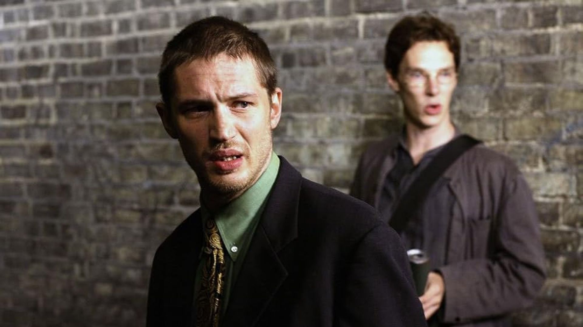 Tom Hardy y Benedict Cumberbatch jóvenes de pie contra una pared de ladrillo