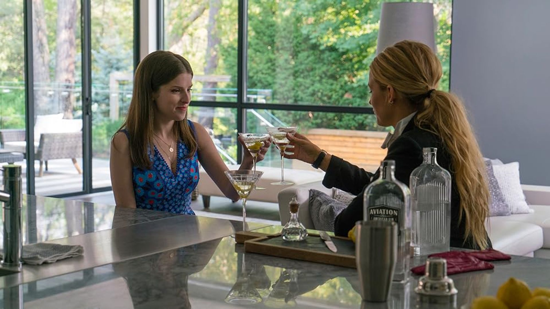 Anna Kendrick y Blake Lively brindando con copas de vino mientras están sentadas en la cocina
