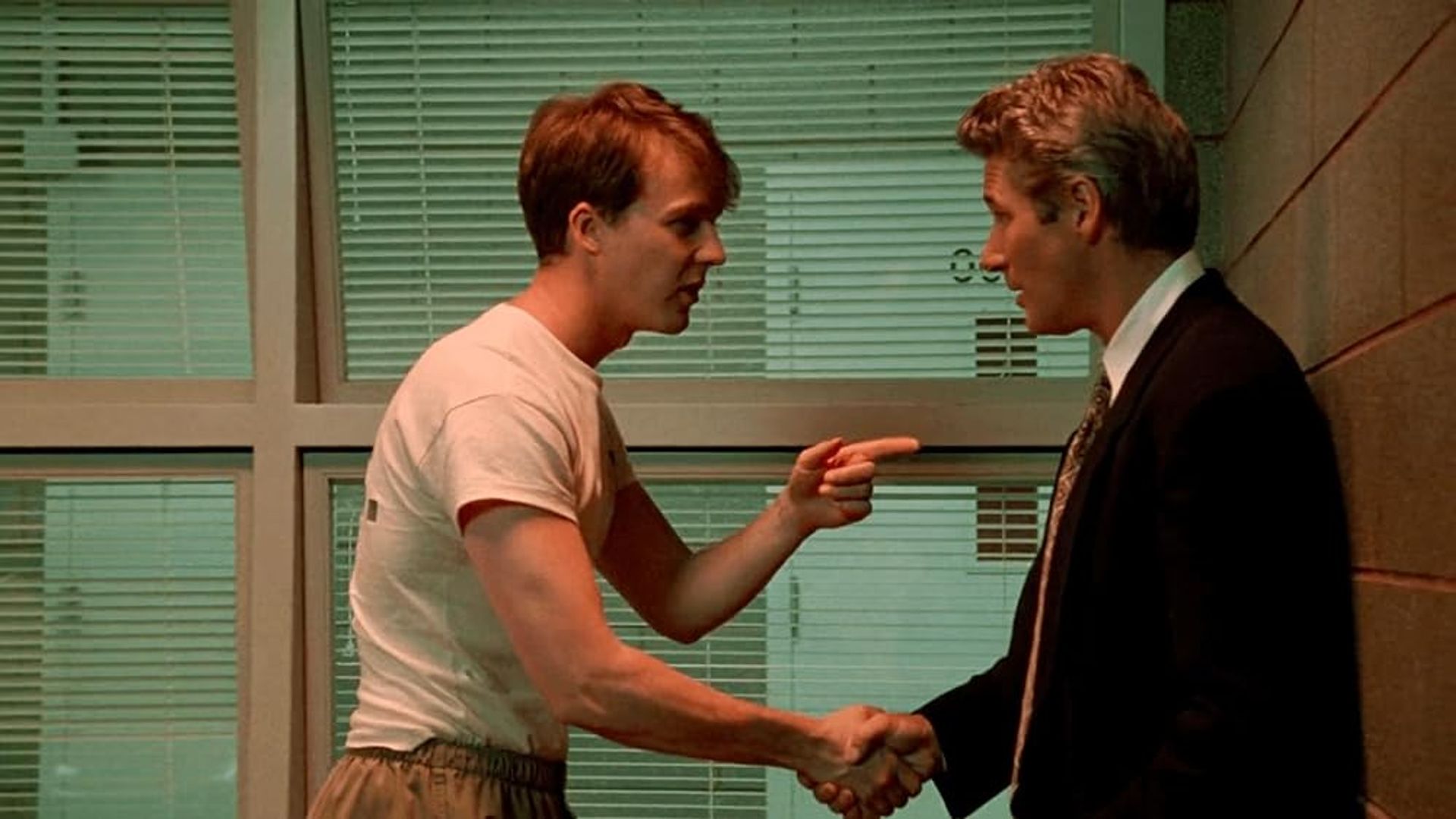 Edward Norton en camiseta estrechando la mano de Richard Gere en traje, señalándolo con el dedo