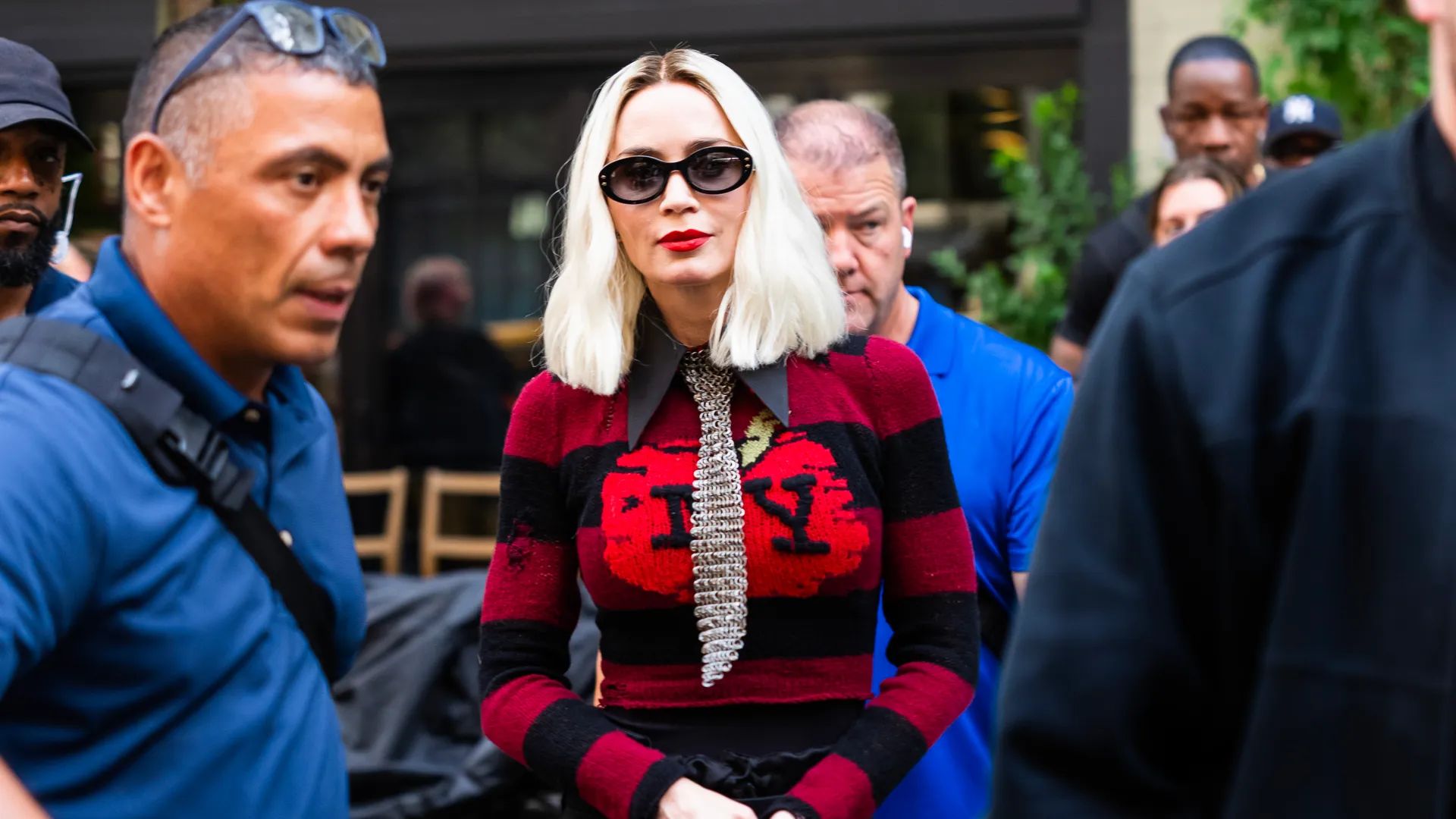 Emily Blunt con bob platinado en suéter rojo con letras NY