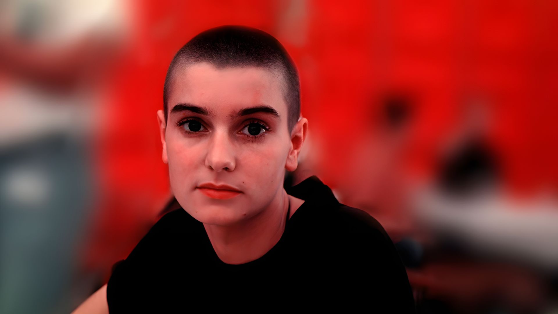 Joven Sinéad O'Connor fotografiada contra un fondo rojo