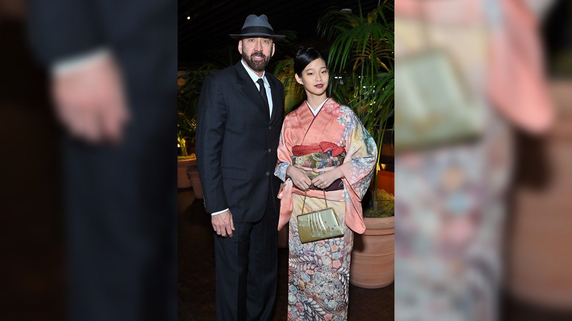 Nicolas Cage con traje negro y sombrero y Riko Shibata con kimono rosa estampado
