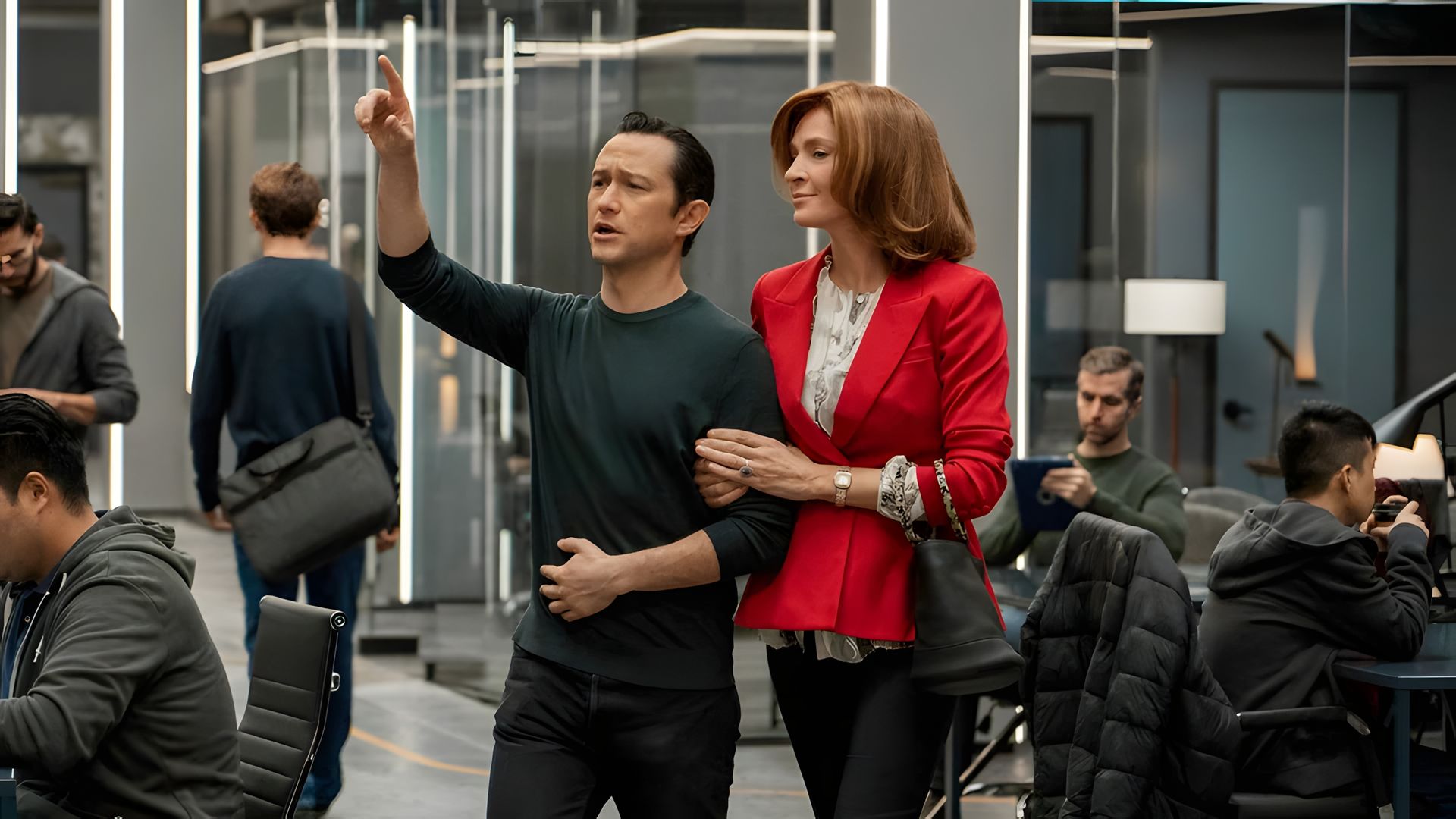Joseph Gordon-Levitt con ropa oscura señala hacia adelante mientras Uma Thurman con chaqueta roja se agarra de su brazo