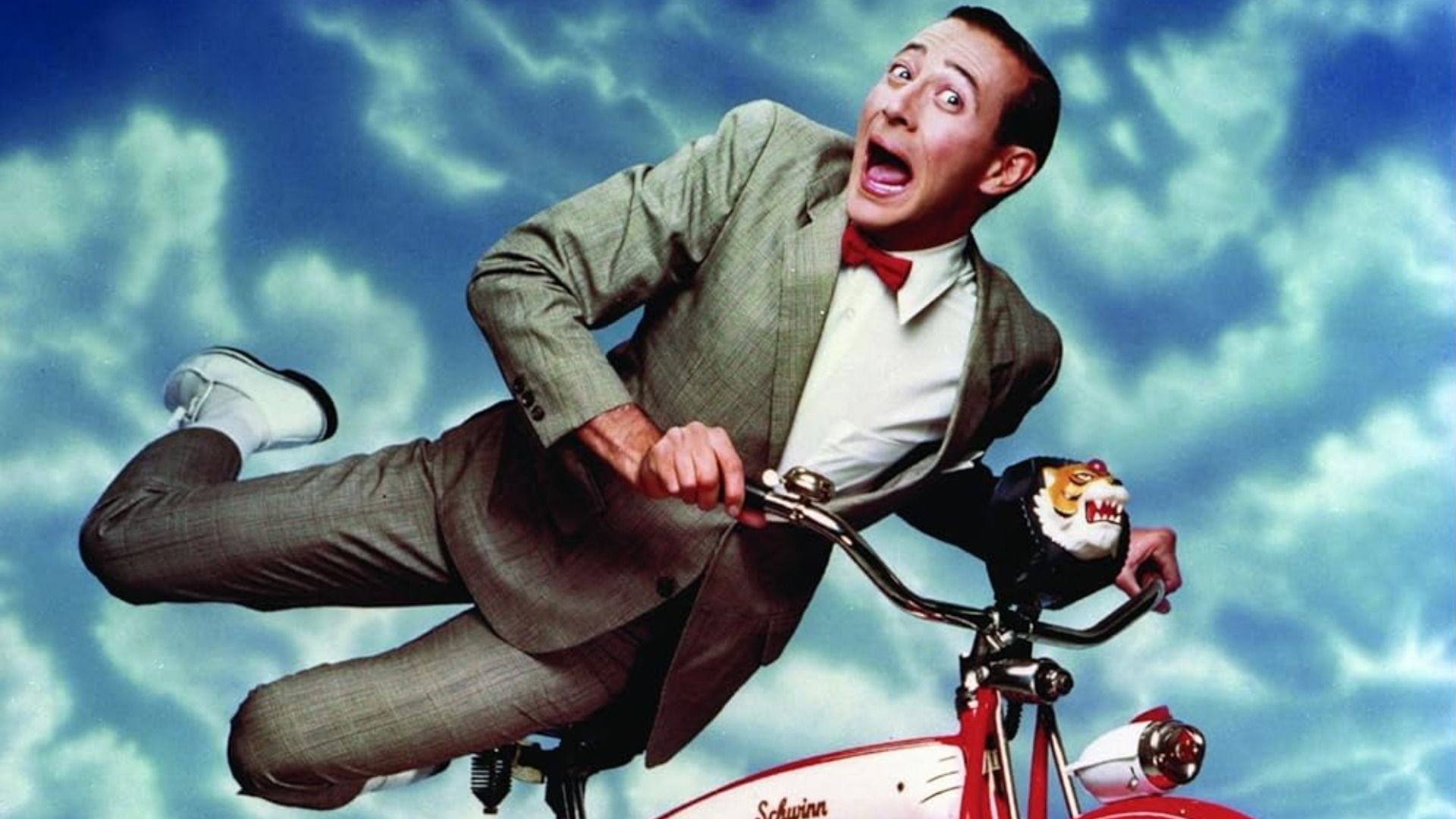 Actor y comediante Paul Reubens en traje gris sobre una bicicleta