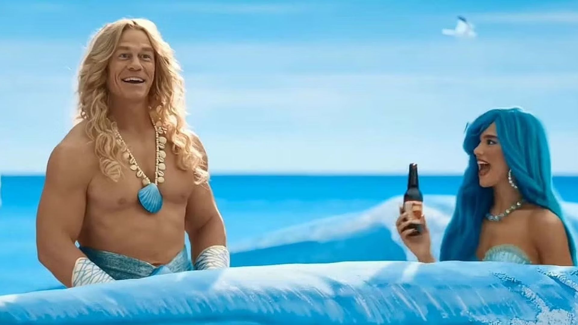 John Cena y Dua Lipa en trajes de sirena nadando a través de olas pintadas