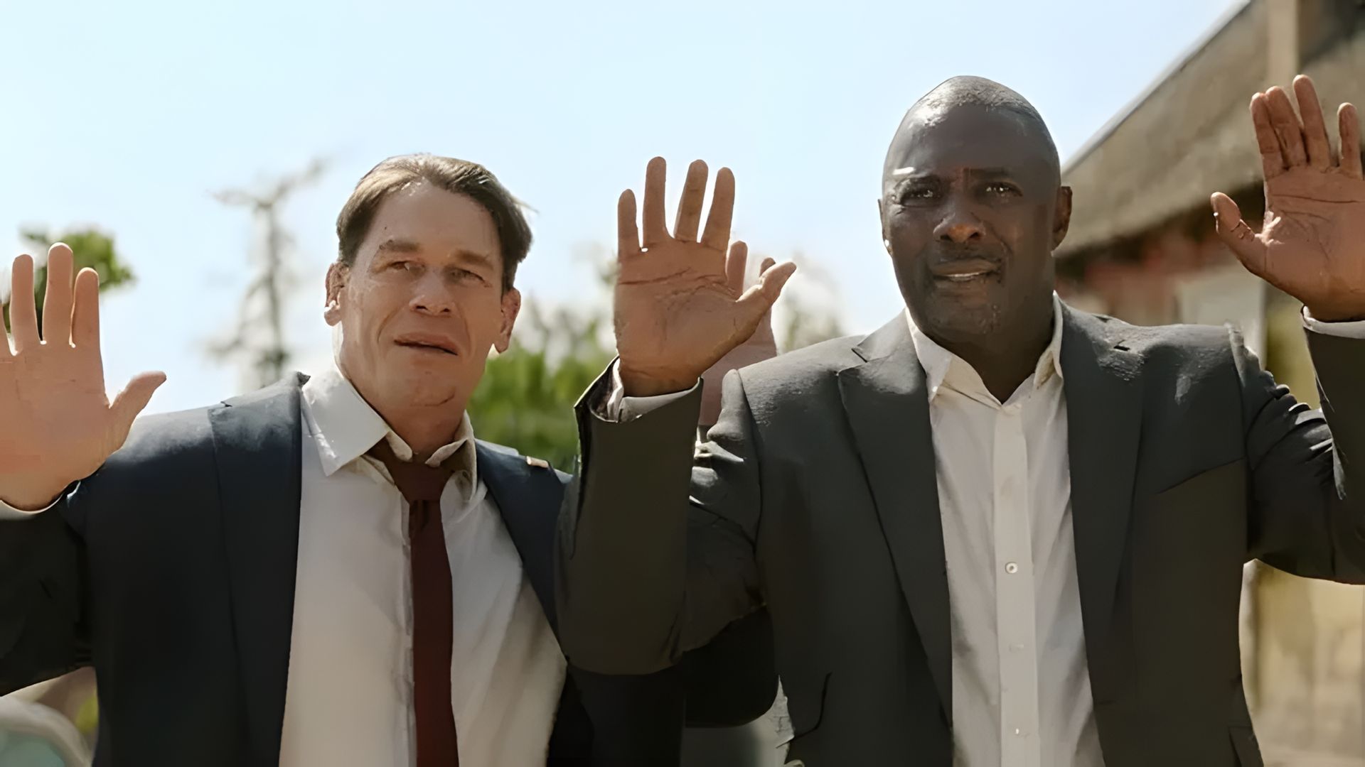 John Cena e Idris Elba en trajes levantando las manos, escena de una película de acción