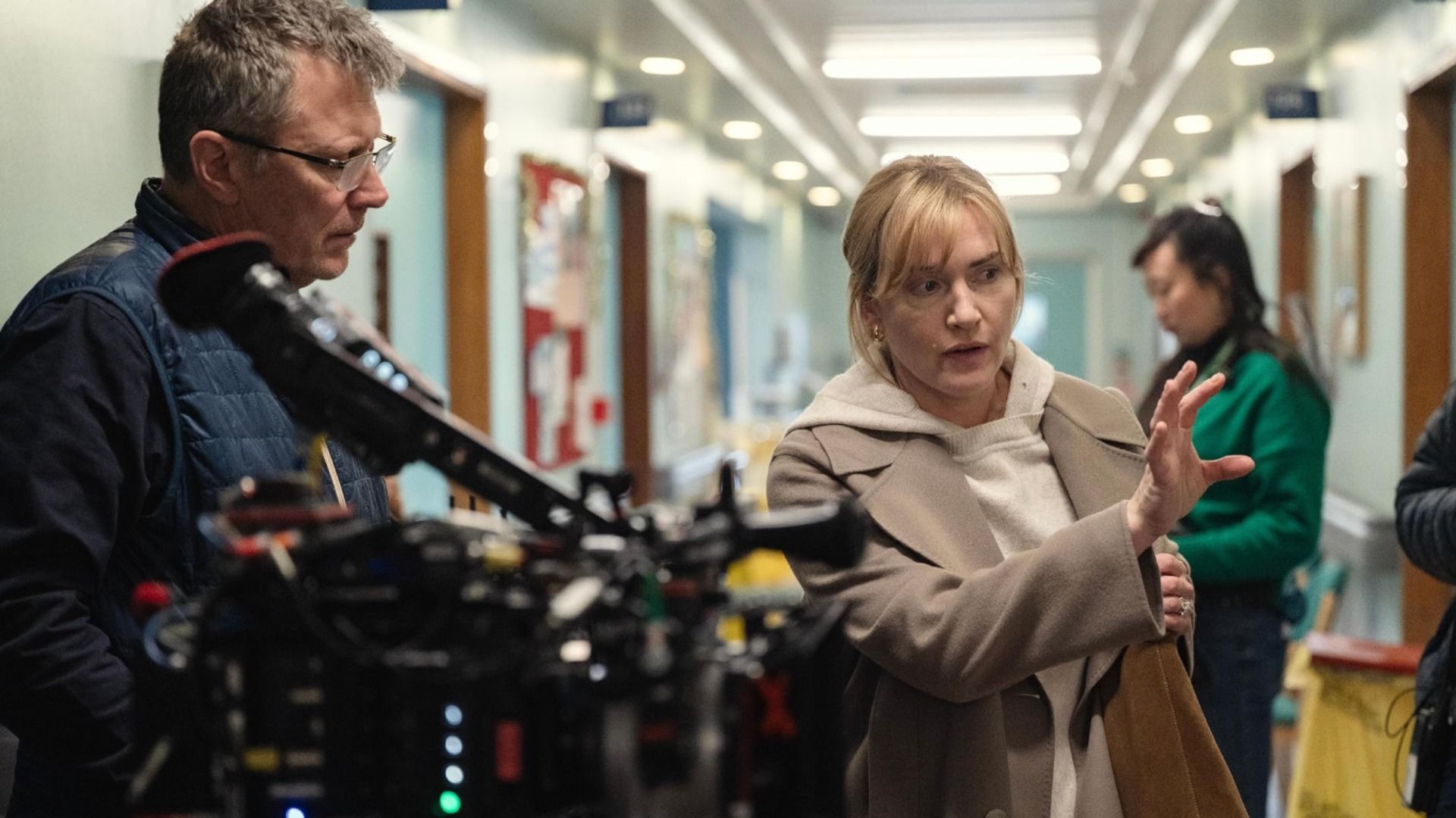 La actriz Kate Winslet con un abrigo beige da indicaciones a un hombre con una cámara