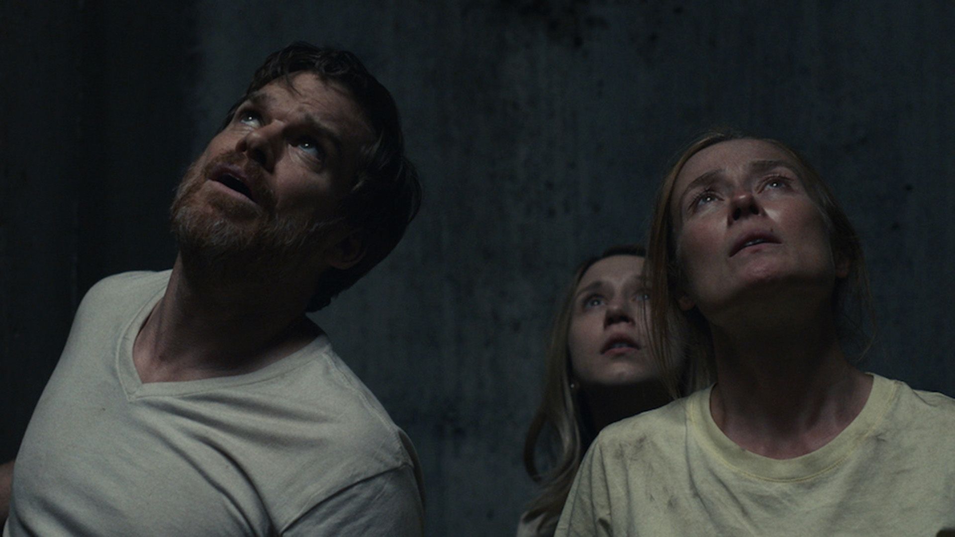 Michael C. Hall y dos mujeres en la oscuridad mirando hacia arriba