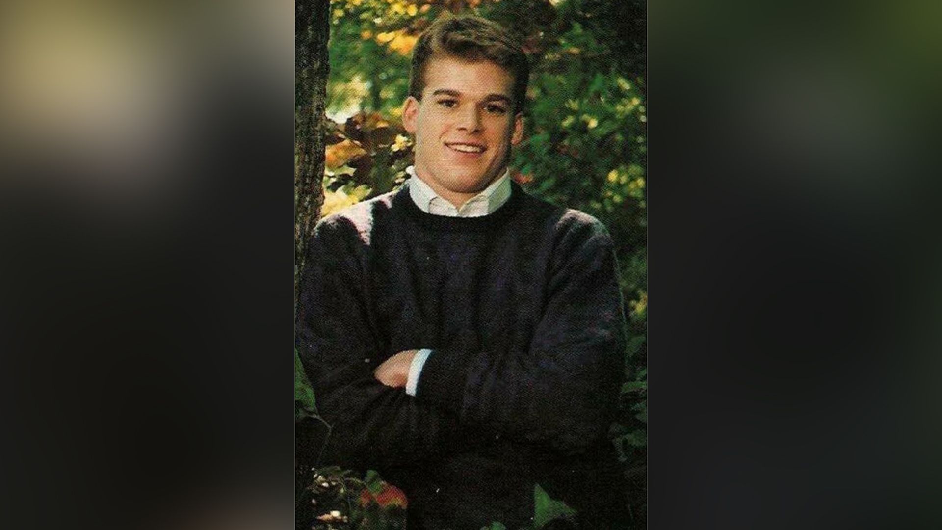 Michael C. Hall joven está de pie con los brazos cruzados sobre el pecho, sonriendo ampliamente