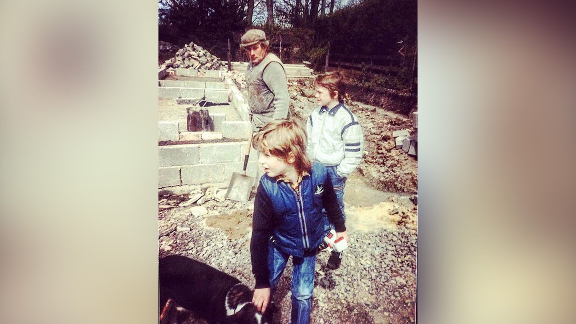 El pequeño Tom Hardy acaricia a un perro en el jardín con su primo y abuelo cerca