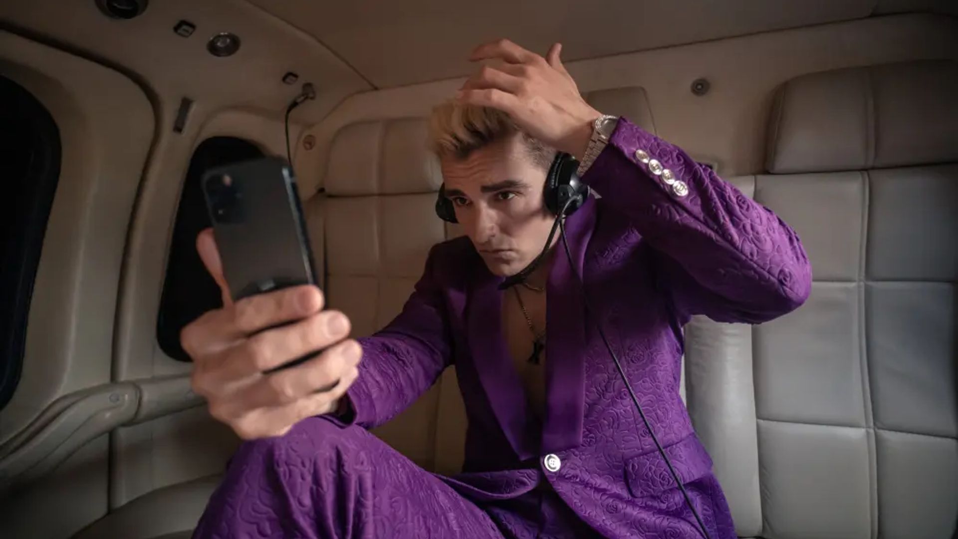 Dave Franco con un traje morado mirando su teléfono, escena de la serie The Afterparty