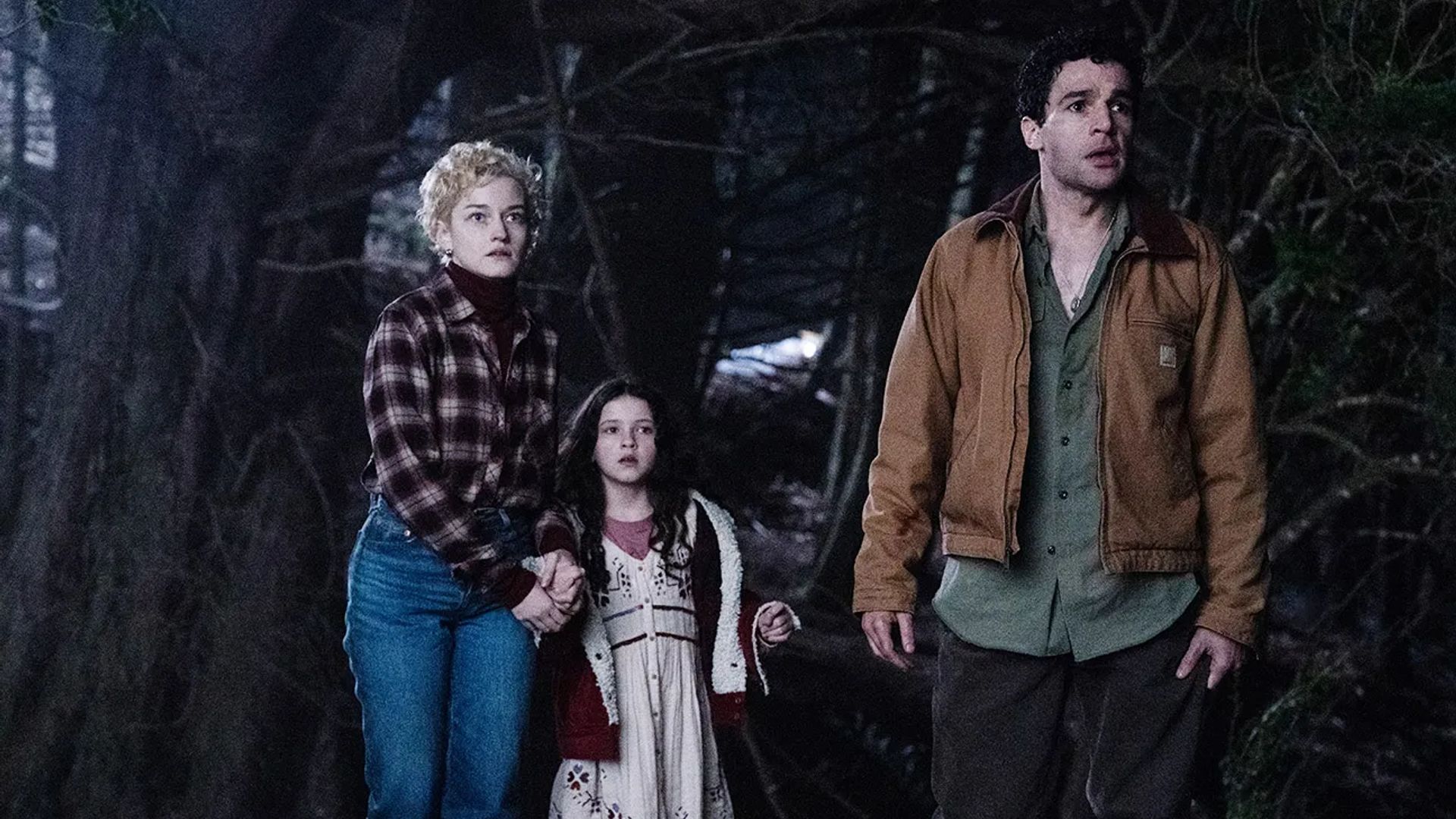 Julia Garner, Christopher Abbott y Matilda Firth en un bosque nocturno, fotograma de la película "Wolf Man"