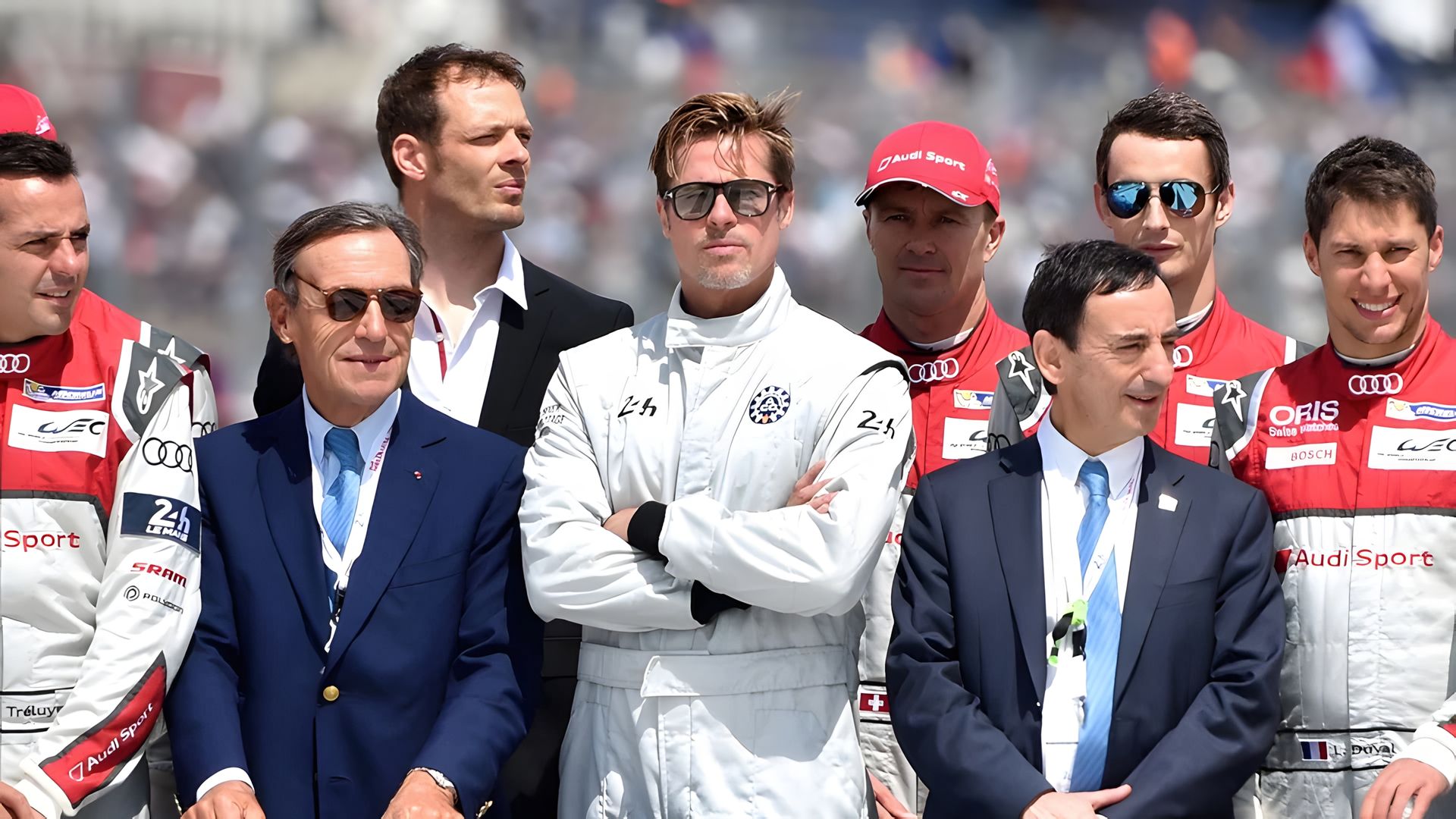 Brad Pitt con equipo de piloto de carreras está de pie rodeado por su equipo