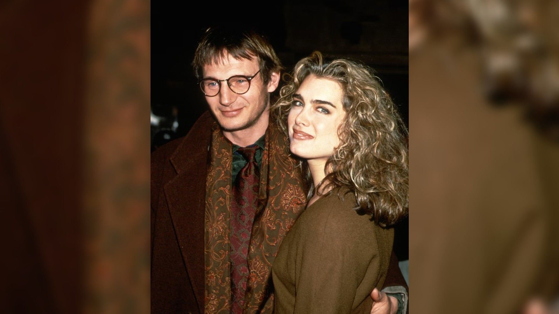 Liam Neeson y Brooke Shields en su juventud, abrazándose y caminando hacia adelante