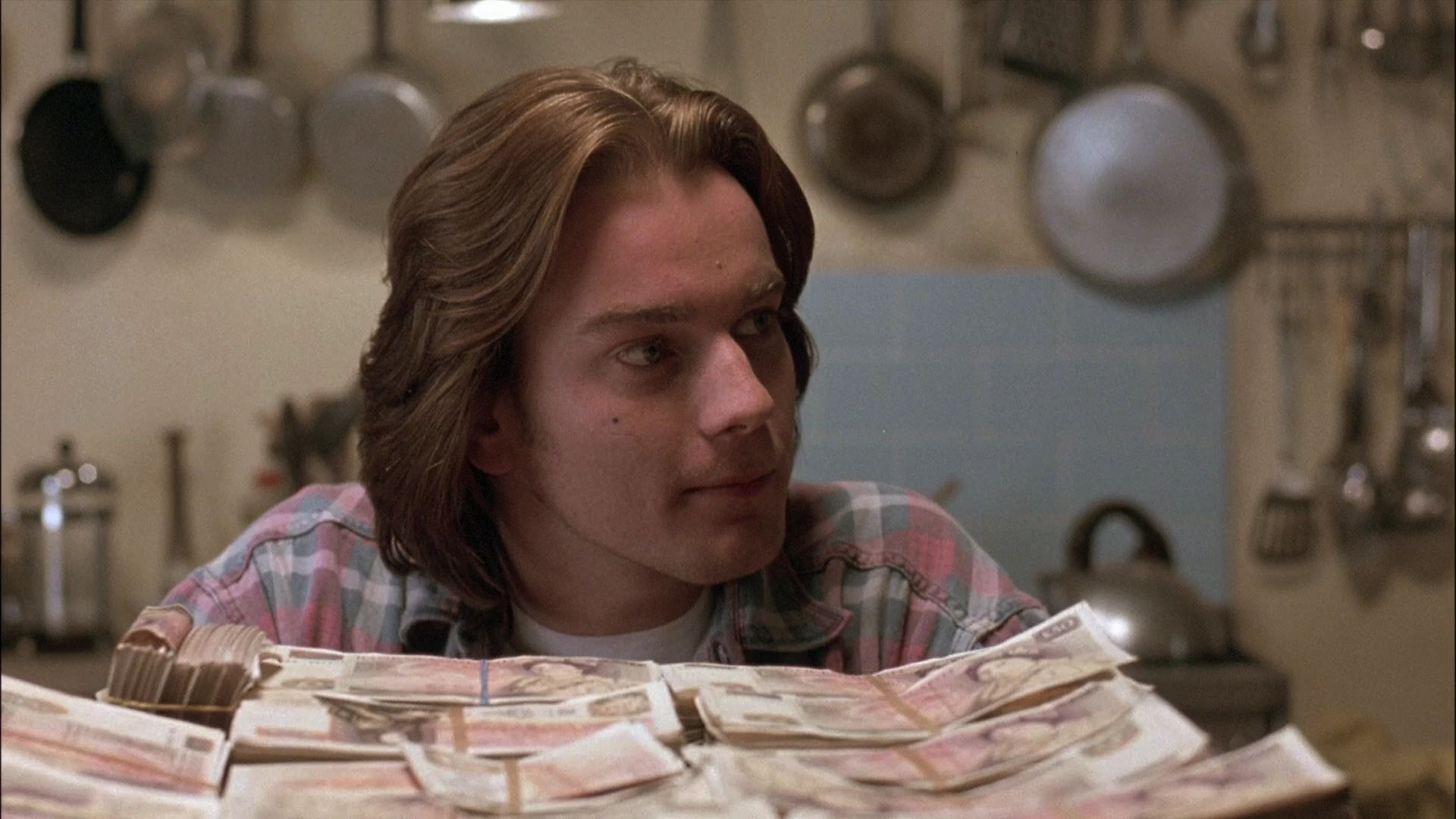 Joven Ewan McGregor con pelo largo mirando un fajo de dinero