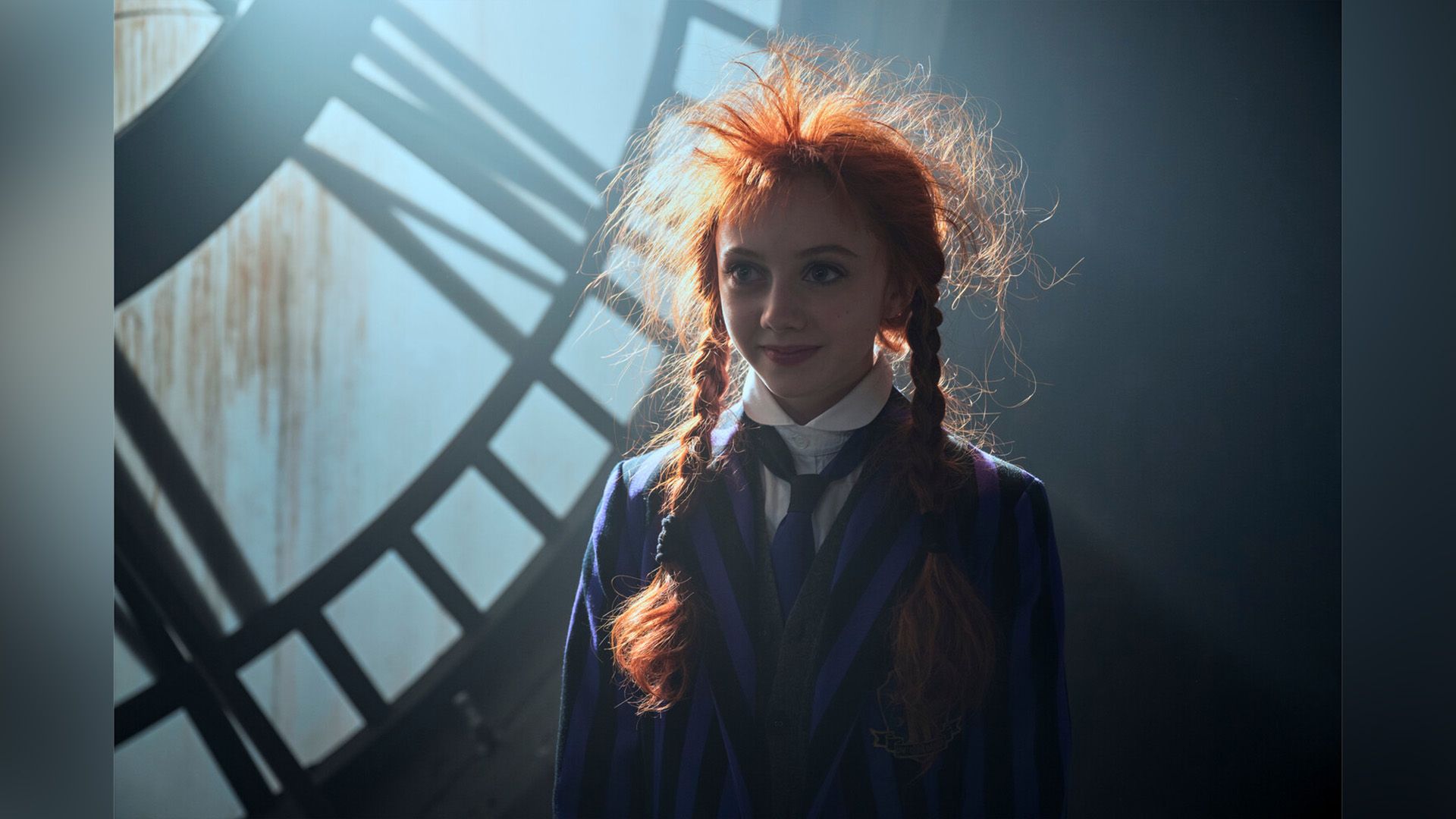 Evie Templeton con trenzas rojas y cabello despeinado, llevando un blazer a rayas negras y moradas