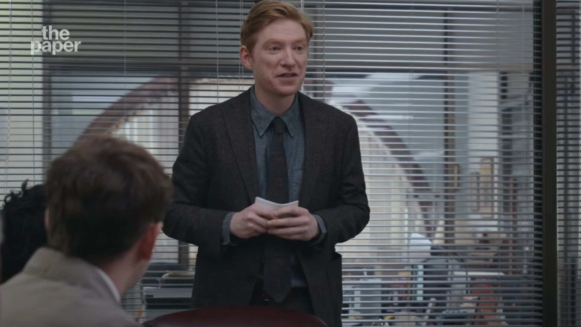 Domhnall Gleeson en traje de pie en una sala de conferencias