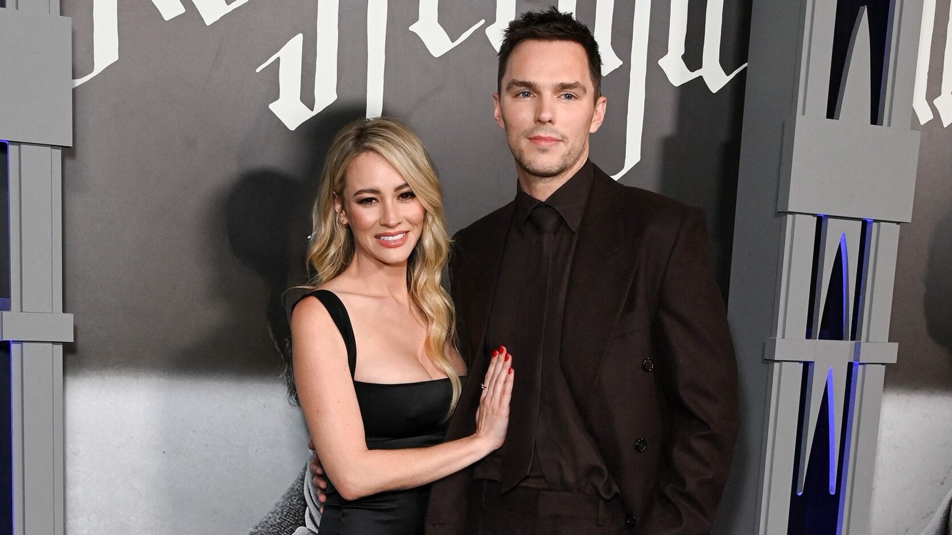 Nicholas Hoult en traje oscuro y Bryana Holly en vestido negro posan juntos en la alfombra roja