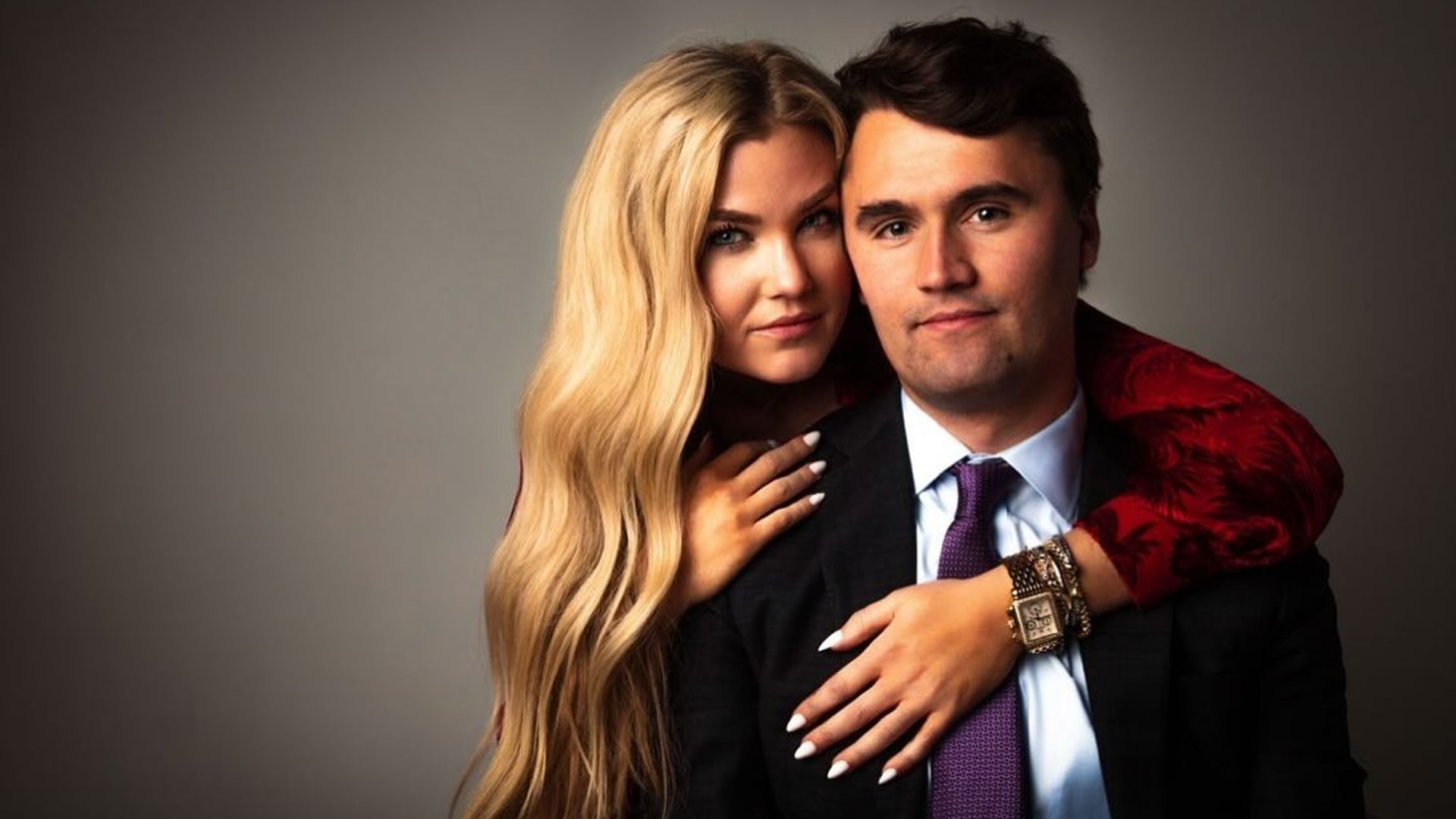 Charlie Kirk y Erica Frantzve se abrazan frente a la cámara contra un fondo oscuro