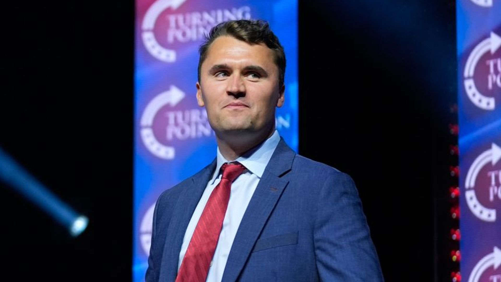 Charlie Kirk posa con orgullo contra un fondo oscuro vistiendo un traje azul