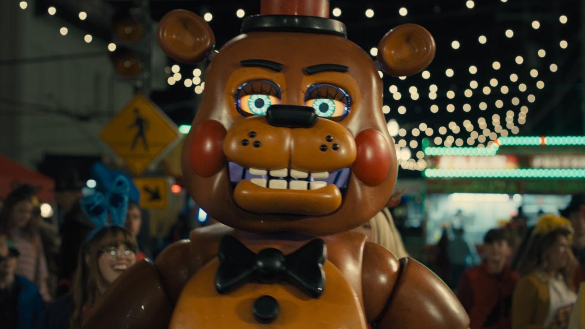 Un animatrónico en forma de oso sonriente parado rodeado de gente