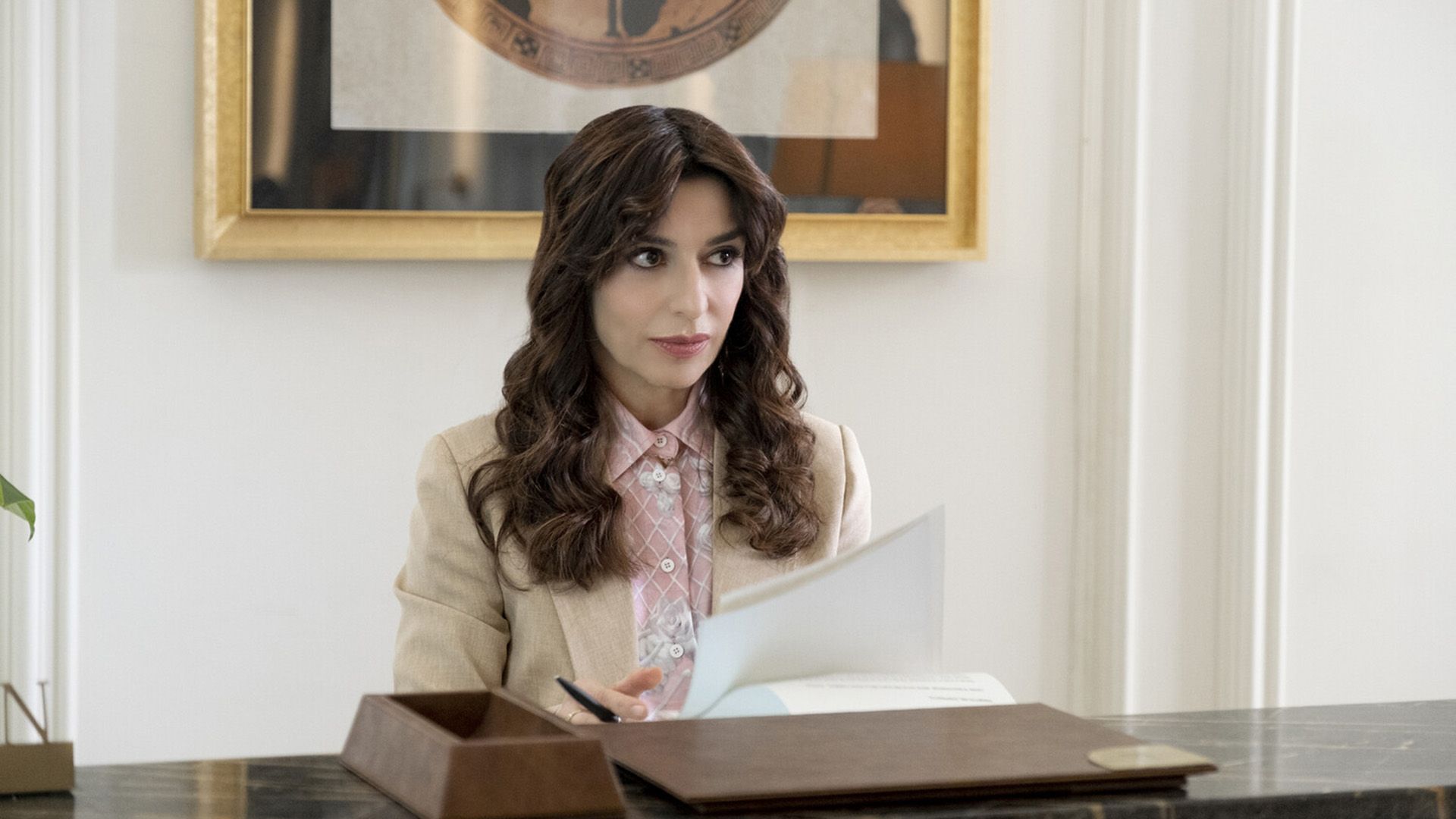 Sabrina Impacciatore con un blazer beige sosteniendo un bolígrafo y papel