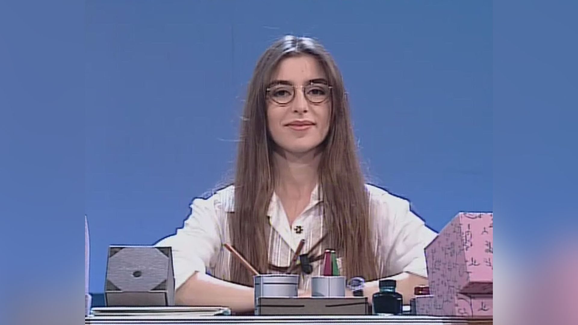 La joven Sabrina Impacciatore con gafas y blusa blanca sentada en un escritorio