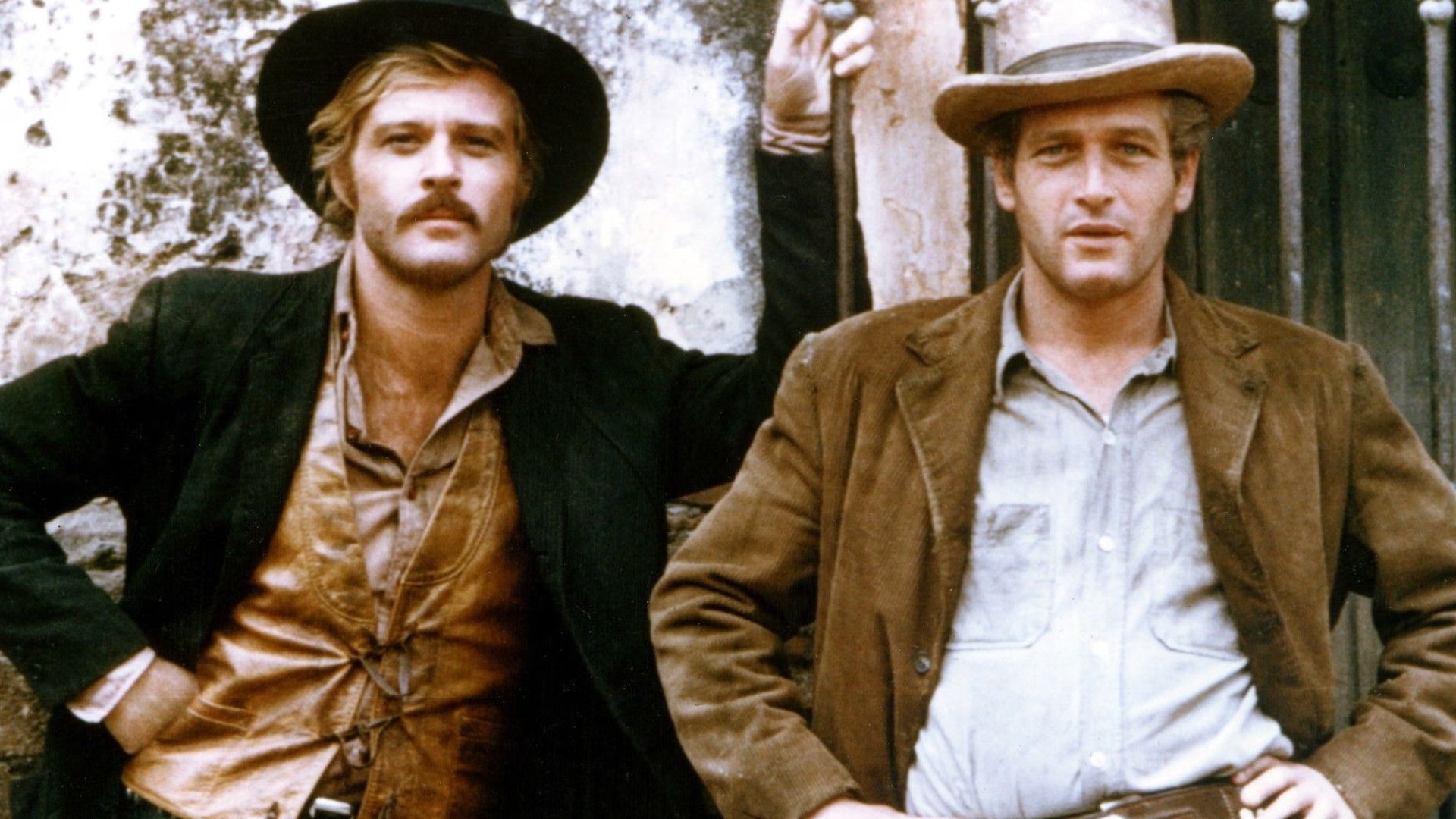 Robert Redford y Paul Newman con sombreros de vaquero y chaquetas de pie uno al lado del otro contra una pared, posando para una foto