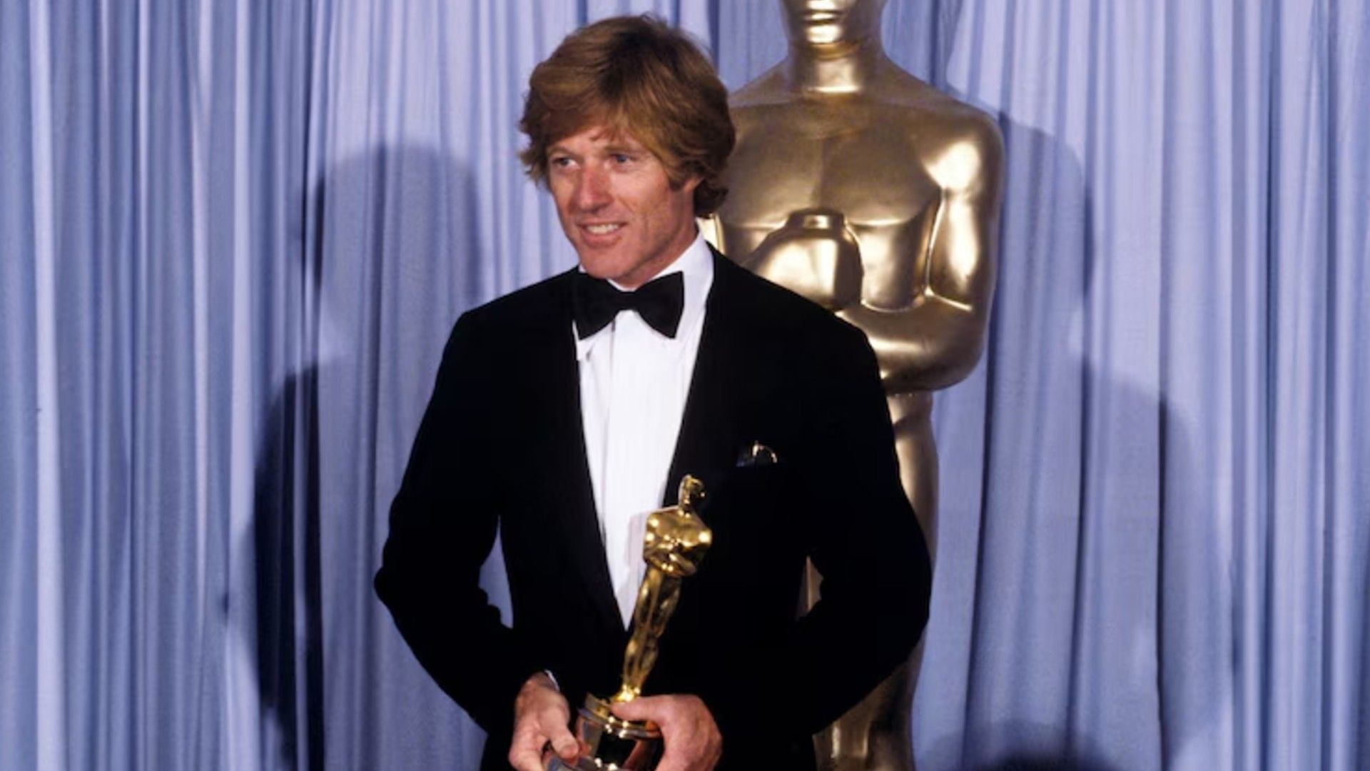 Robert Redford con traje en el escenario sosteniendo un Oscar