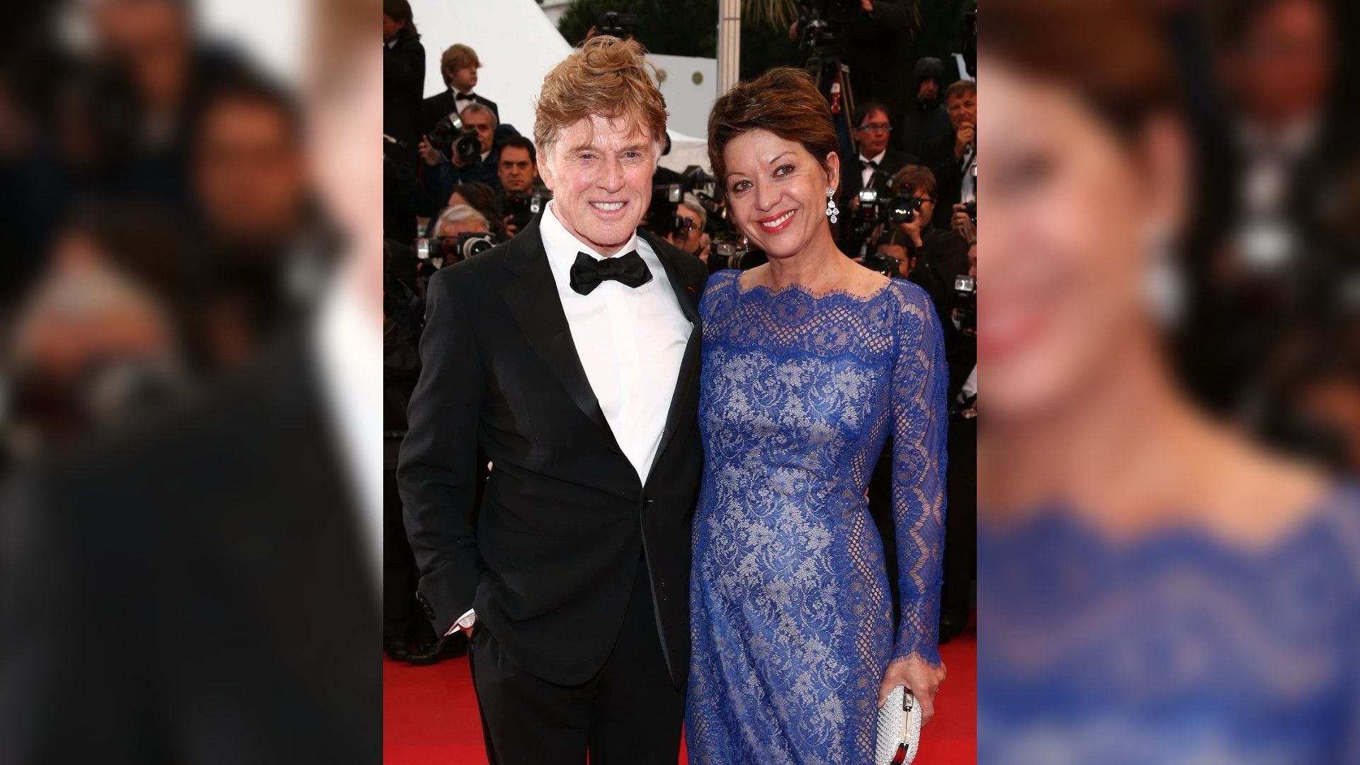 Robert Redford en esmoquin y Sibylle Szaggars en un vestido azul de encaje posan en la alfombra roja rodeados de fotógrafos