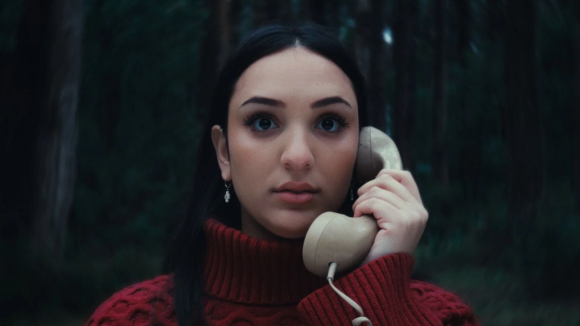 Chica con jersey rojo sosteniendo un auricular de teléfono de pie en el bosque