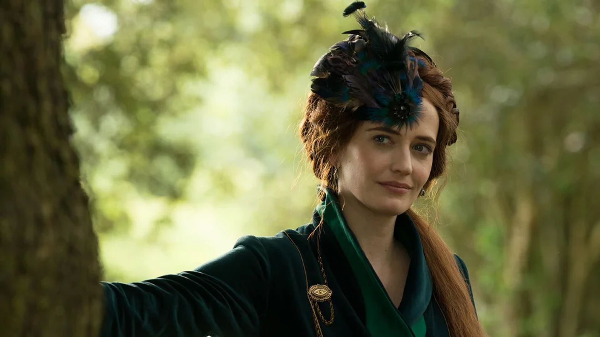 Eva Green con un vestido verde oscuro y adornos de plumas en la cabeza, de pie junto a un árbol contra un fondo de bosque