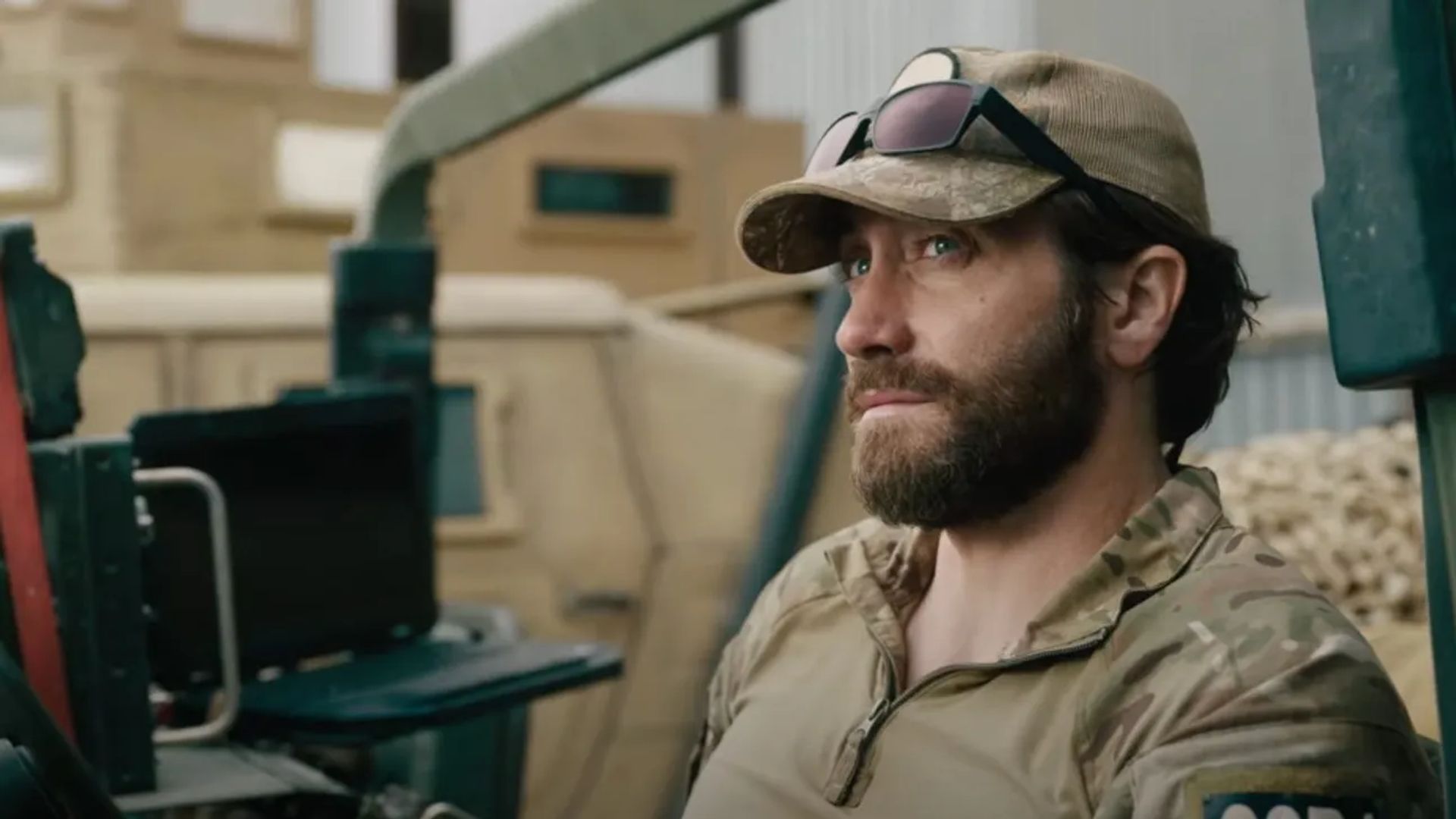 Jake Gyllenhaal en uniforme militar y gorra con gafas en la visera se sienta mirando hacia un lado con expresión seria